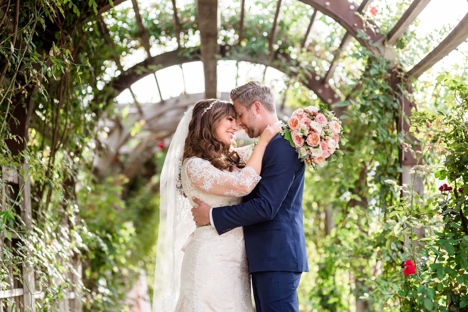A romantic garden wedding at Thanksgiving Point with a couple embracing under a floral archway draped with lush greenery and flowers.