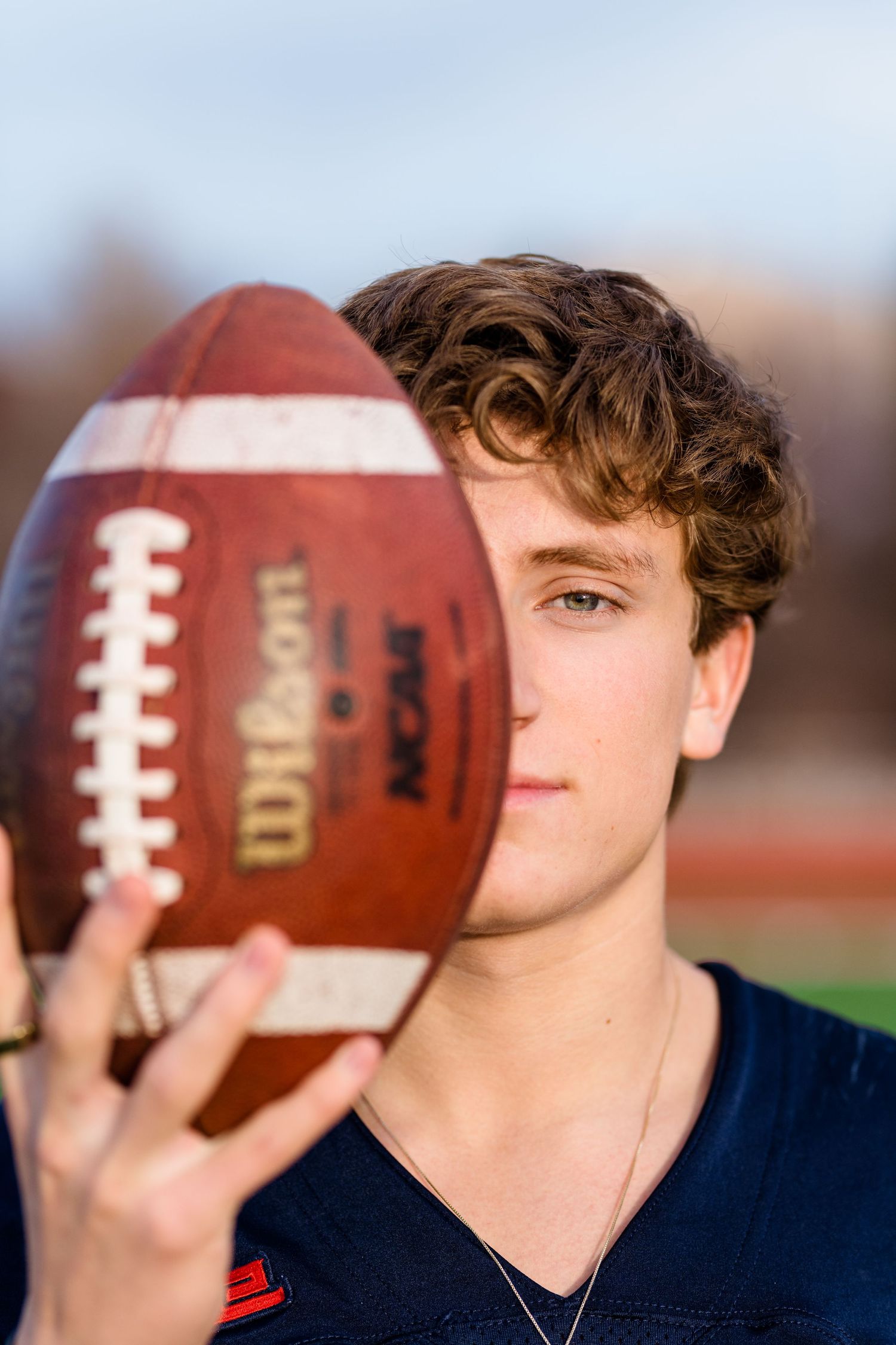 Close-up sequence of a football player holding and positioning a Wilson football against blue jersey background.