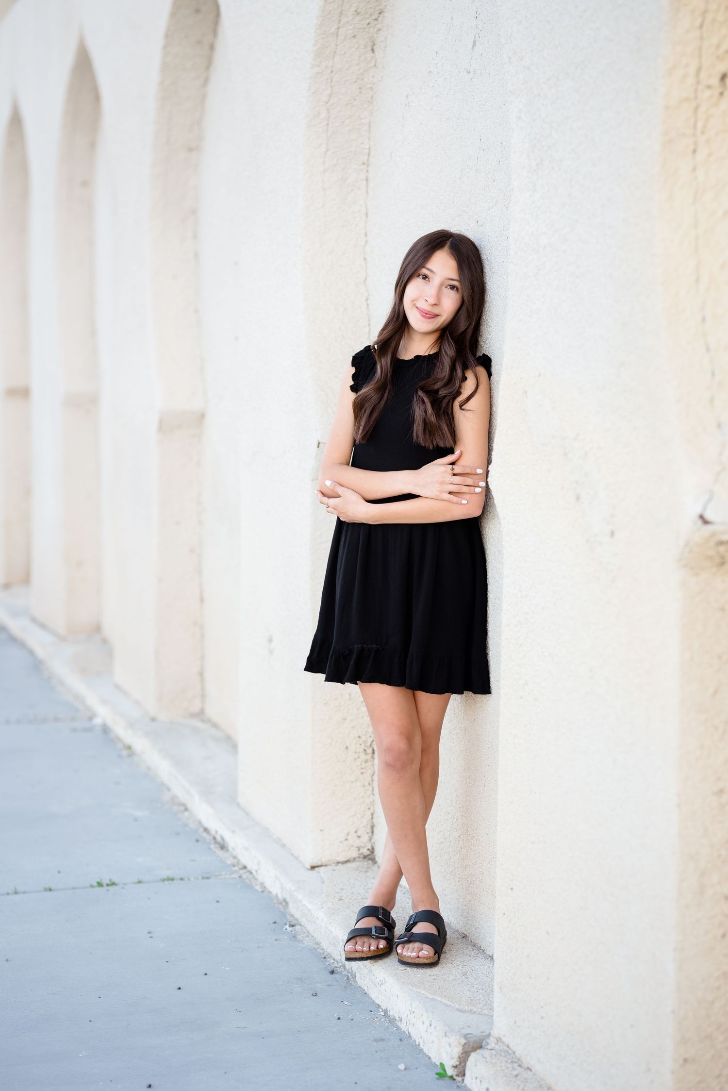 A woman in a black dress poses against white columns in an architectural setting.
