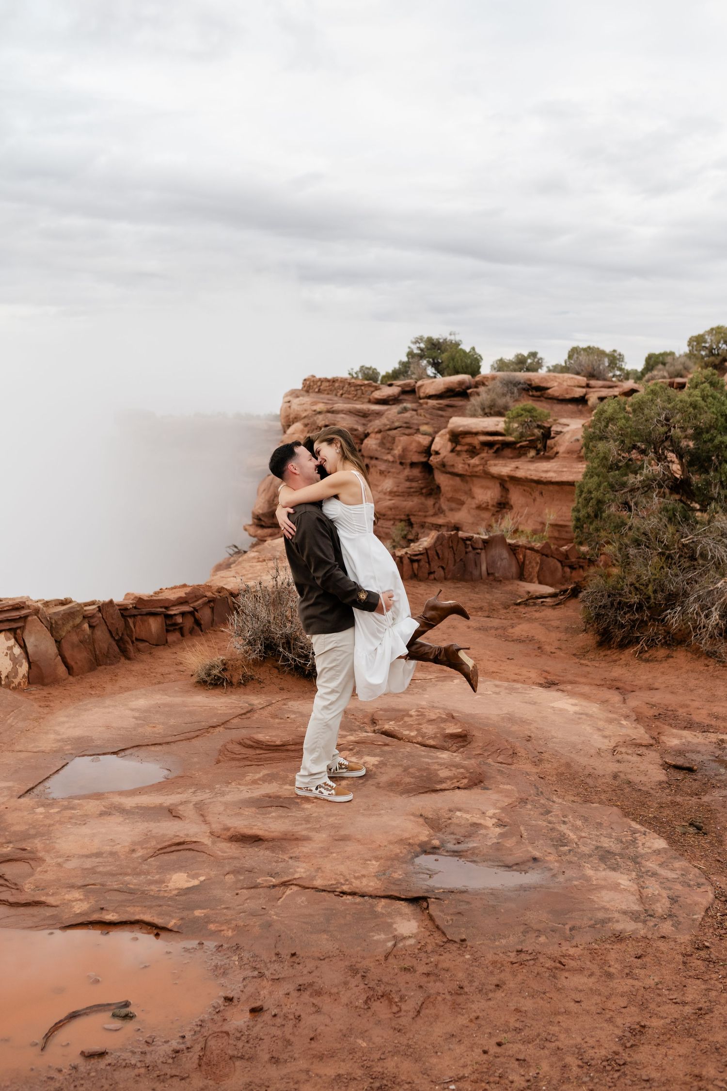 A romantic moment captured on red rock cliffs with dramatic cloudy skies in the background.