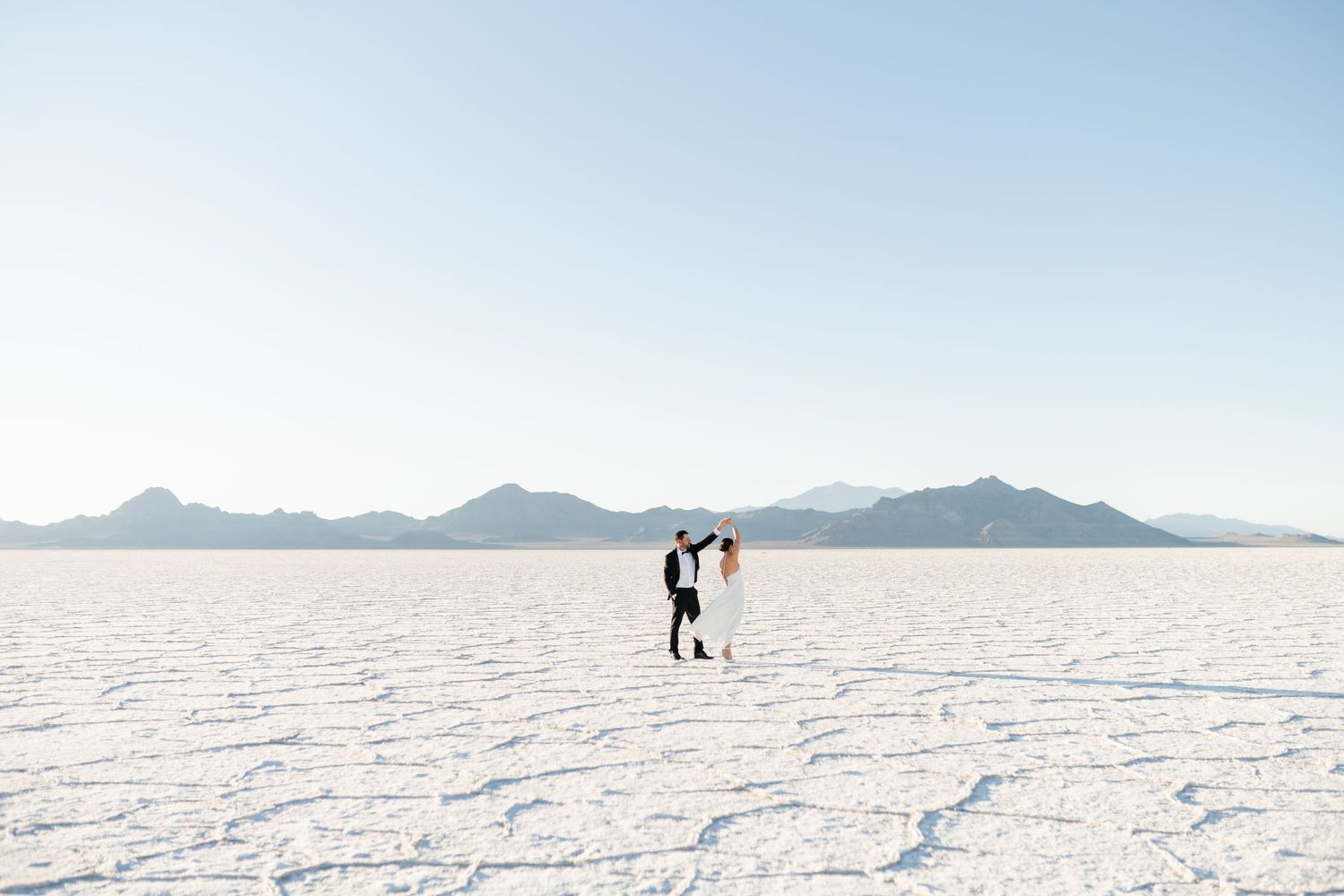 People walk across the vast white expanse of Bonneville Salt Flats with distant mountains on the horizon in Utah. Salt Flats Photographer.