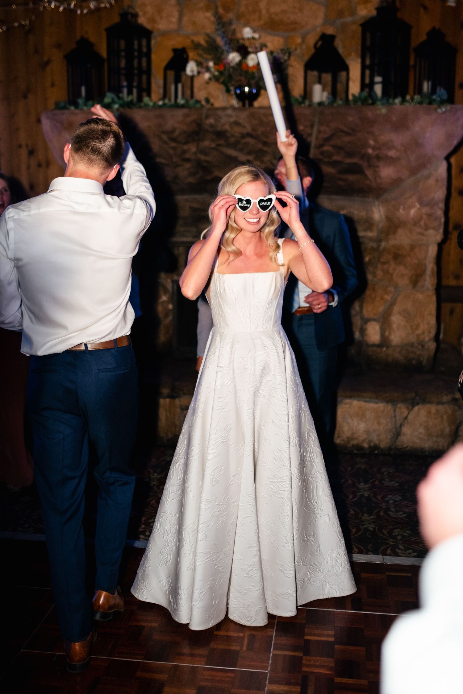 A person in a white wedding dress dances joyfully while wearing heart-shaped sunglasses during the reception. Utah Wedding Photographer.