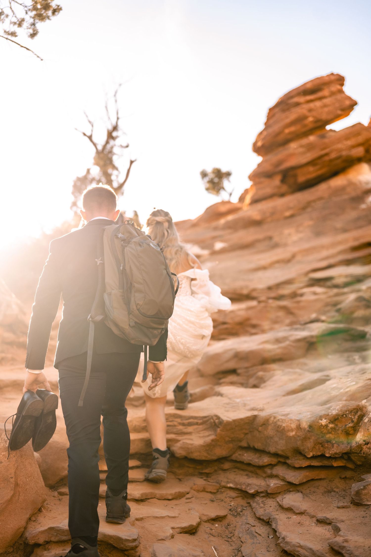 Couple hiking up red rock formations during sunset adventure session.