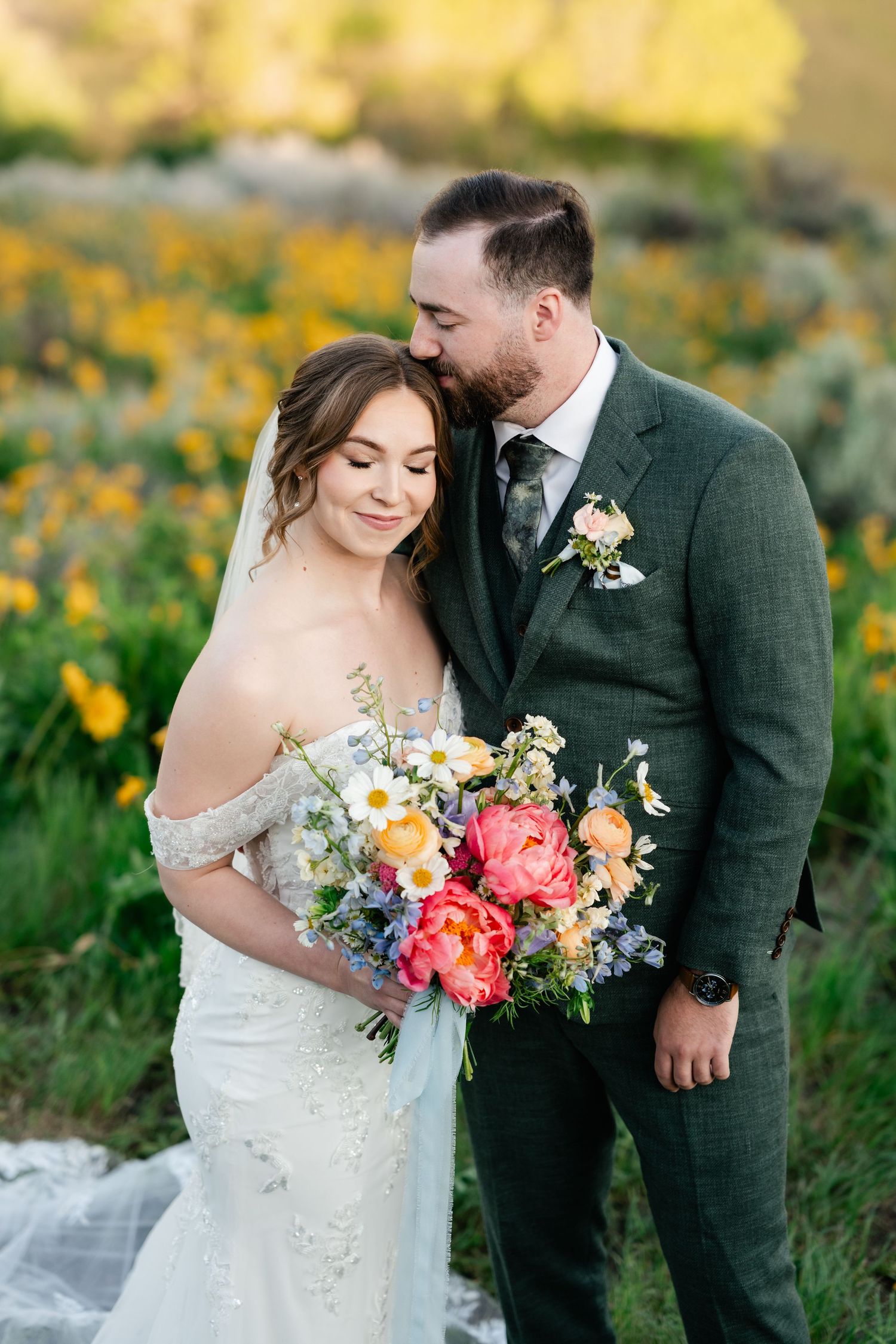 A couple poses in a field of wildflowers with stunning bridal bouquet featuring coral and white blooms.