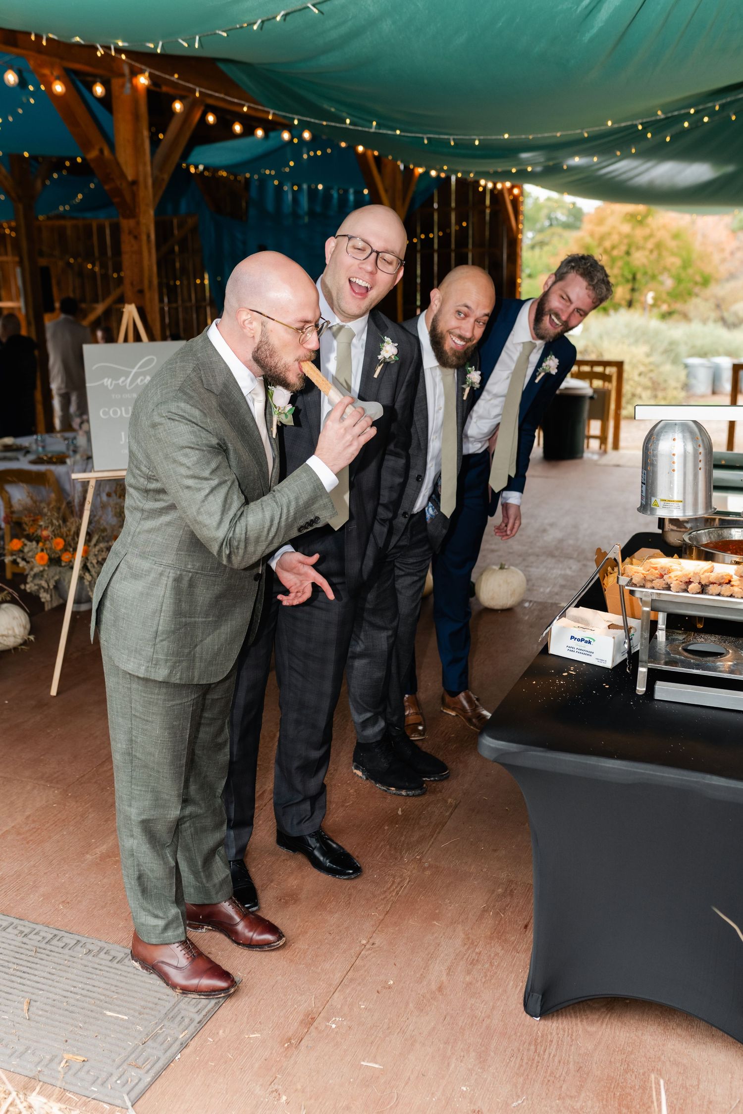 Wedding party members share laughter and dance moves on a rustic wooden dance floor.