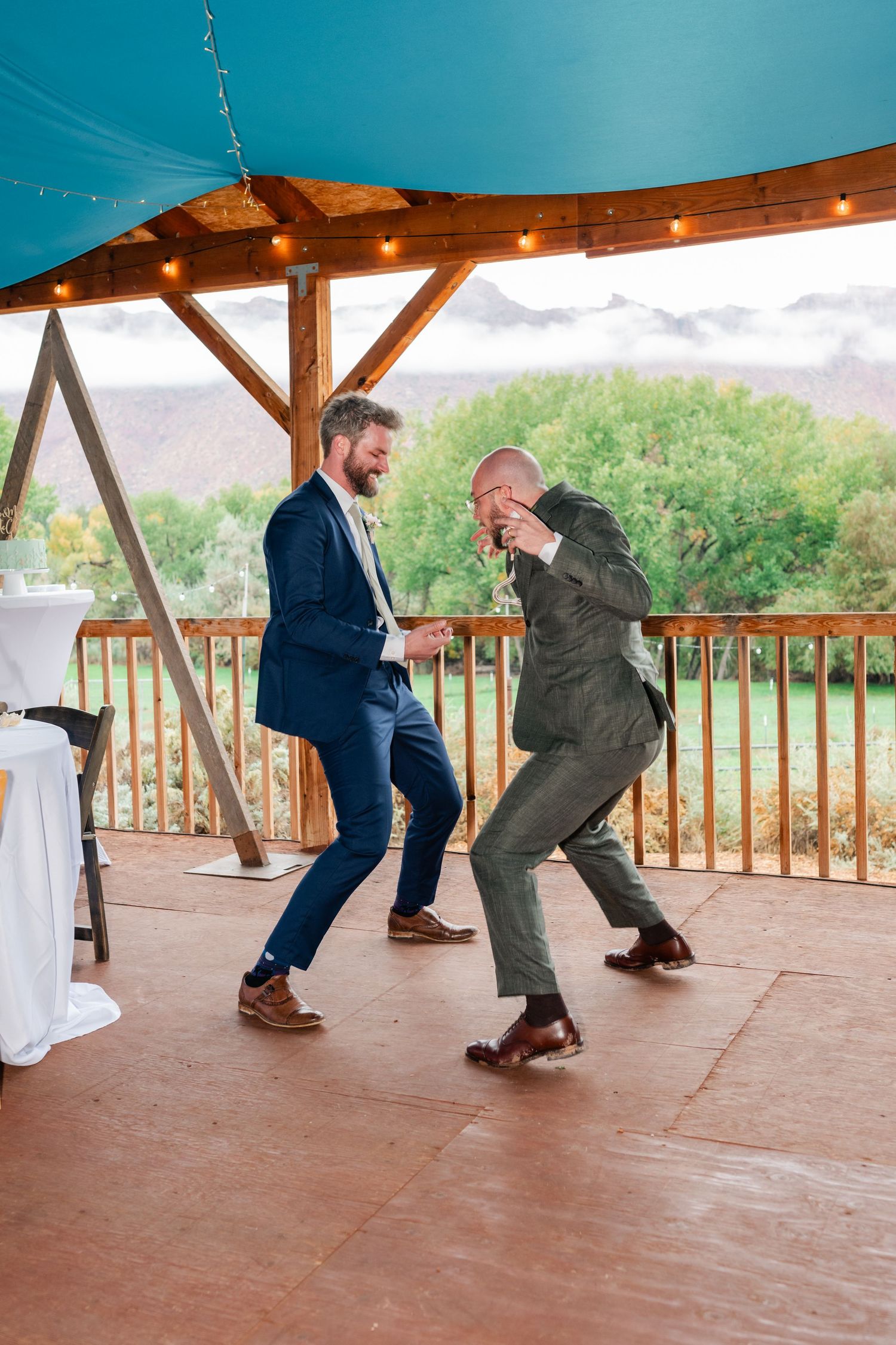 Two guests dancing energetically on a covered patio during a wedding celebration.