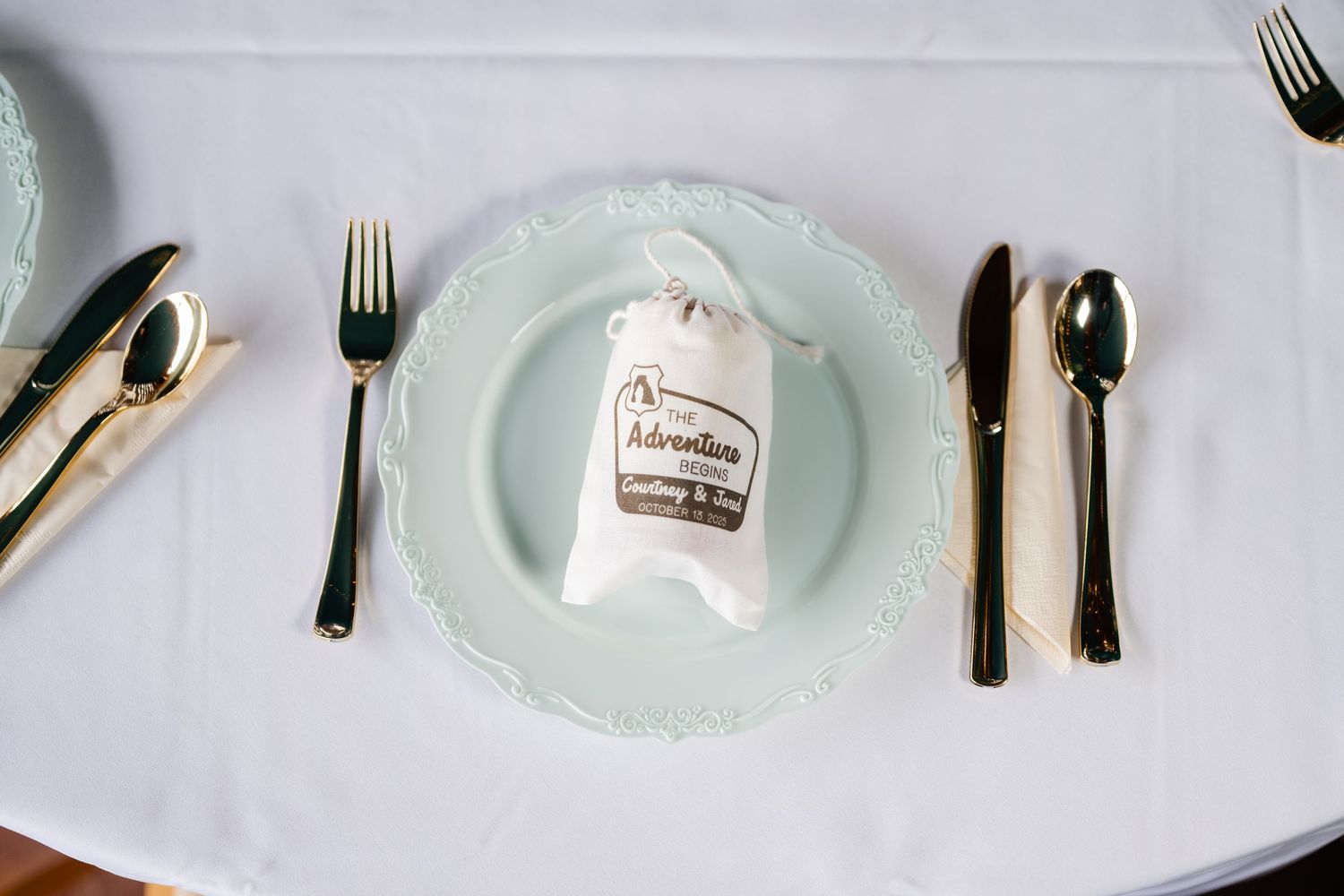 Elegant place setting with mint green plates and silver cutlery on crisp white tablecloth.