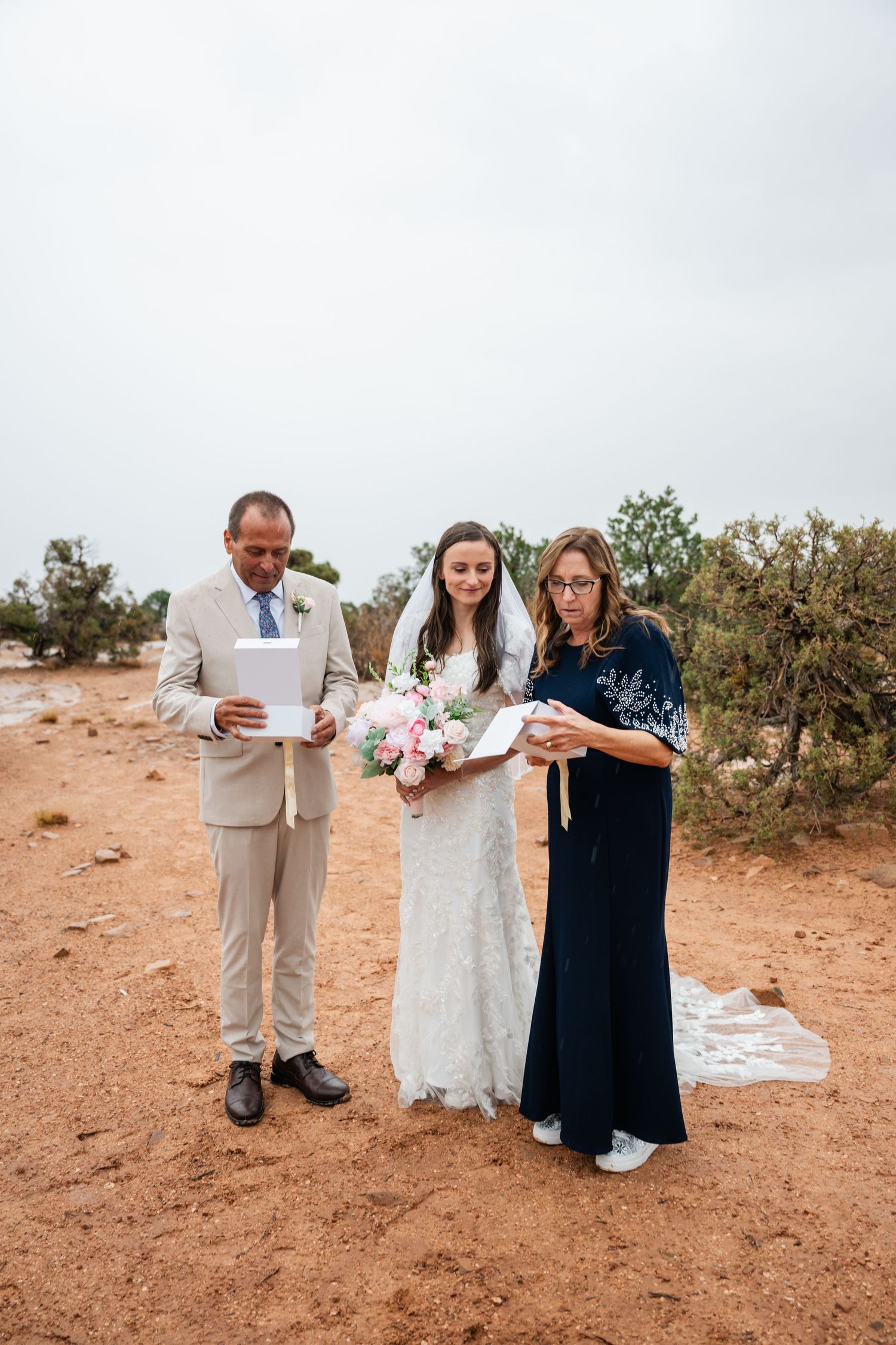 Small wedding ceremony taking place outdoors in a desert setting with attendees in formal attire.