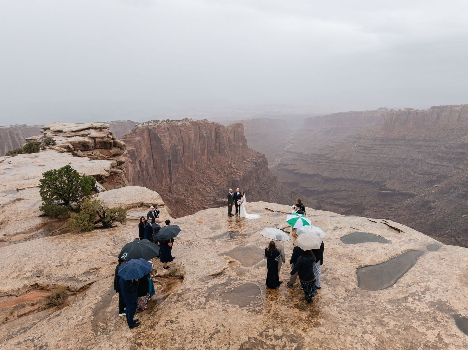 Dramatic desert canyon landscape with people gathered on rocky cliff overlook.