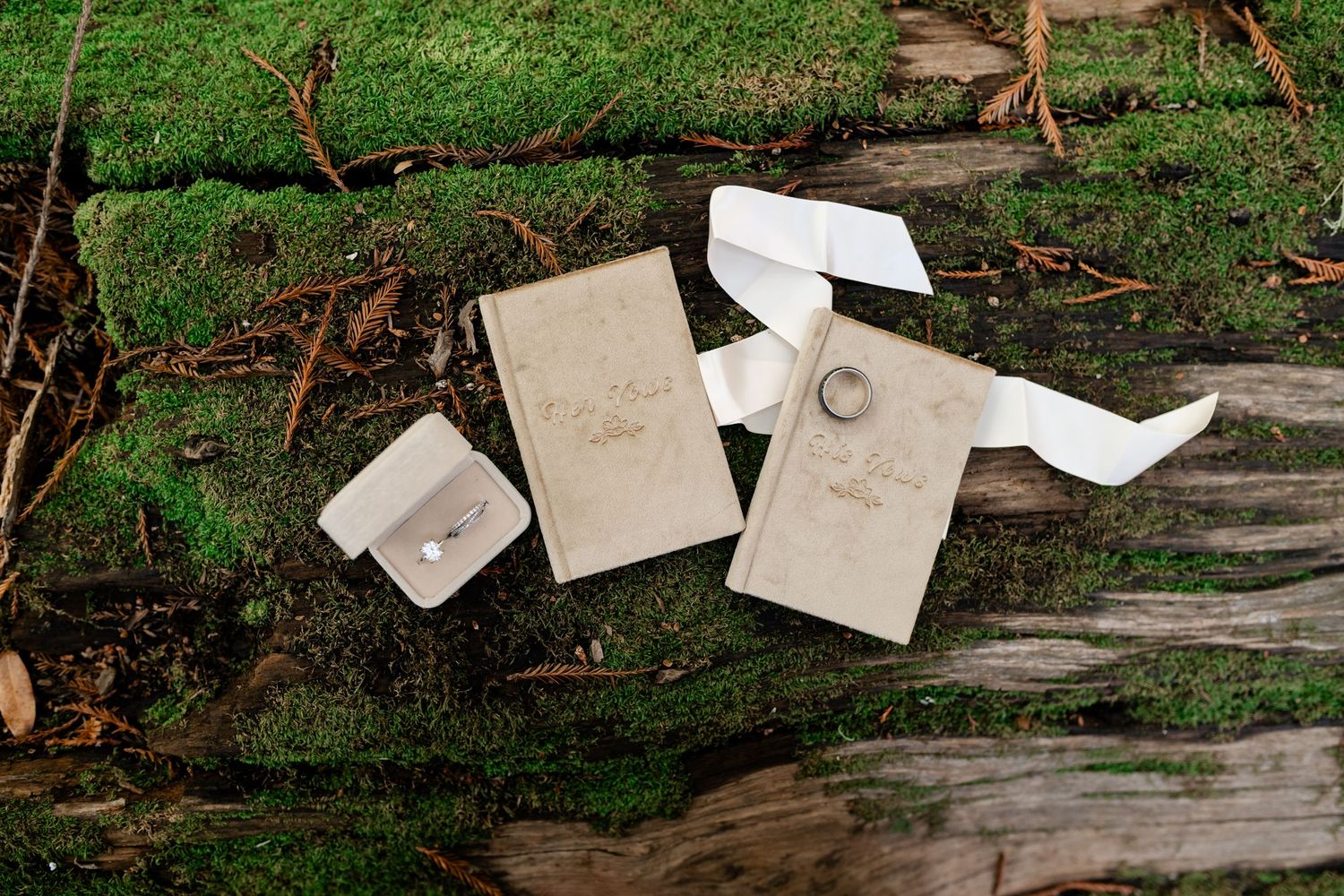 Wedding rings and paper details arranged artistically on weathered wood with moss.