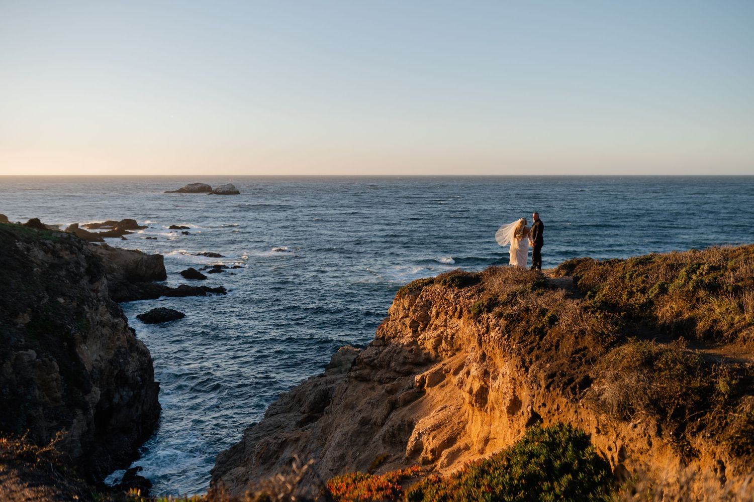 Panoramic view of rugged coastline with waves crashing against cliffs at sunset.