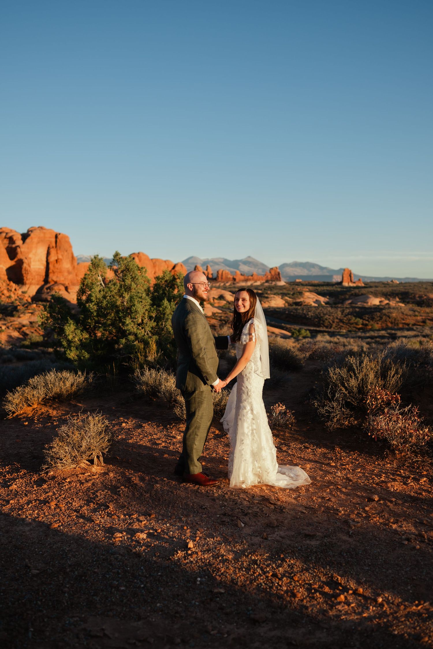 Wedding couple photographed against dramatic red rock formations at sunset in Arches National Park.