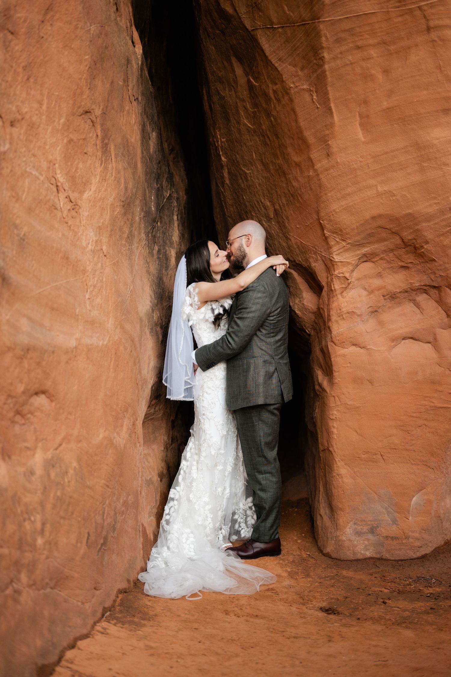 A romantic wedding moment captured in a narrow desert canyon with red rock walls.
