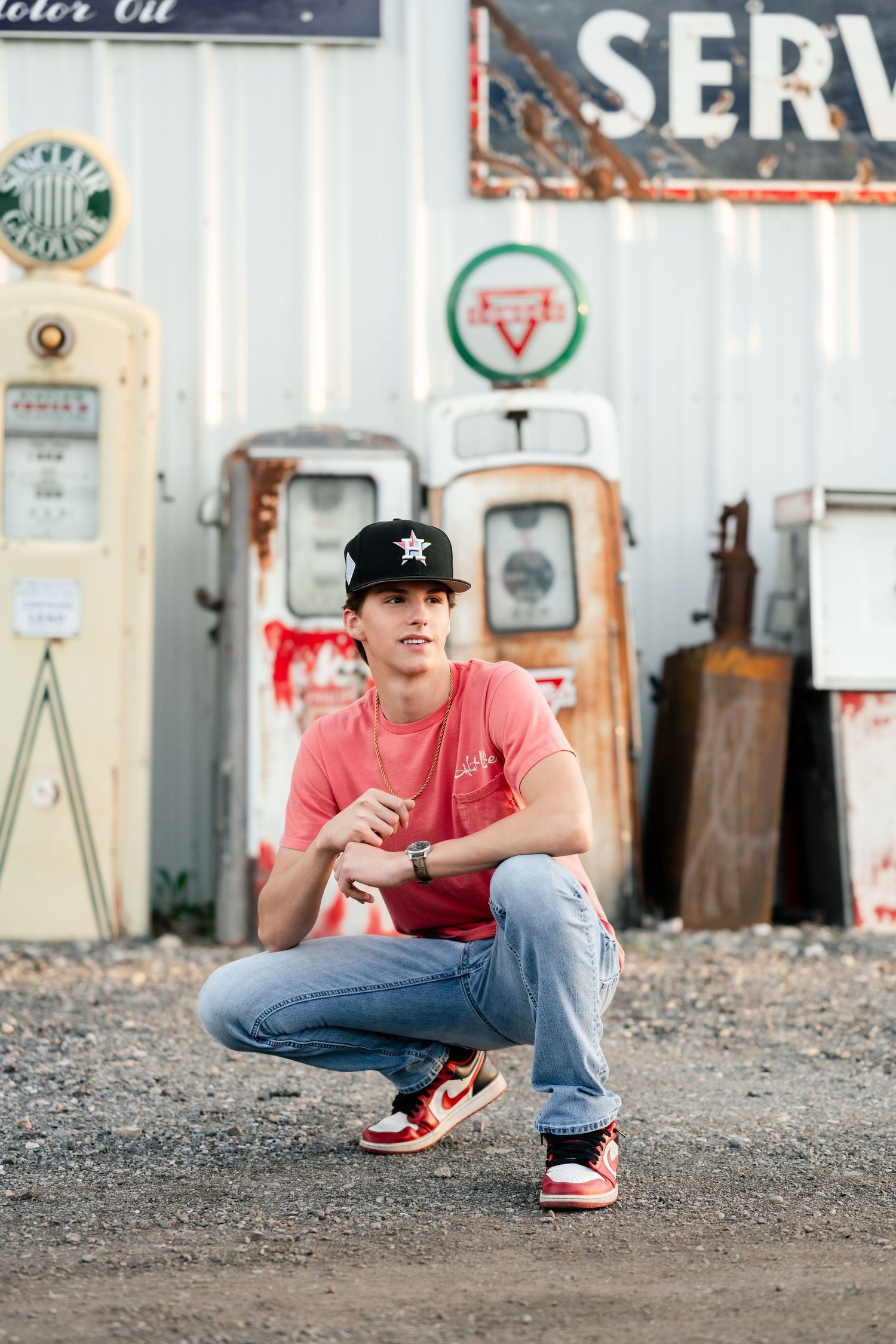 Person in red shirt and baseball cap crouches in front of vintage gas station signs and memorabilia.