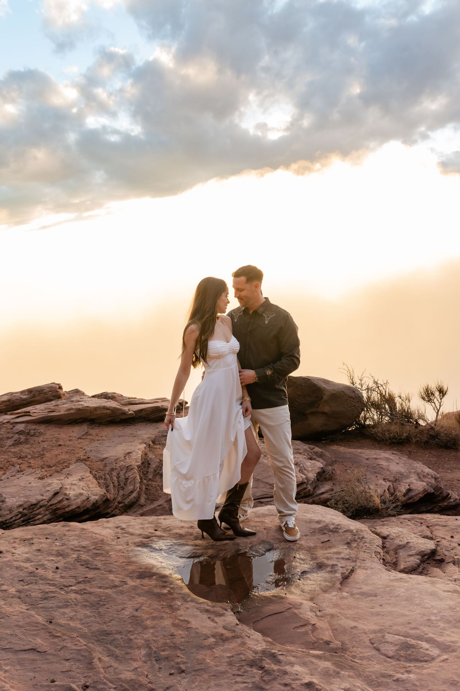 A couple shares tender moments at sunset on red rock formations in a desert setting.