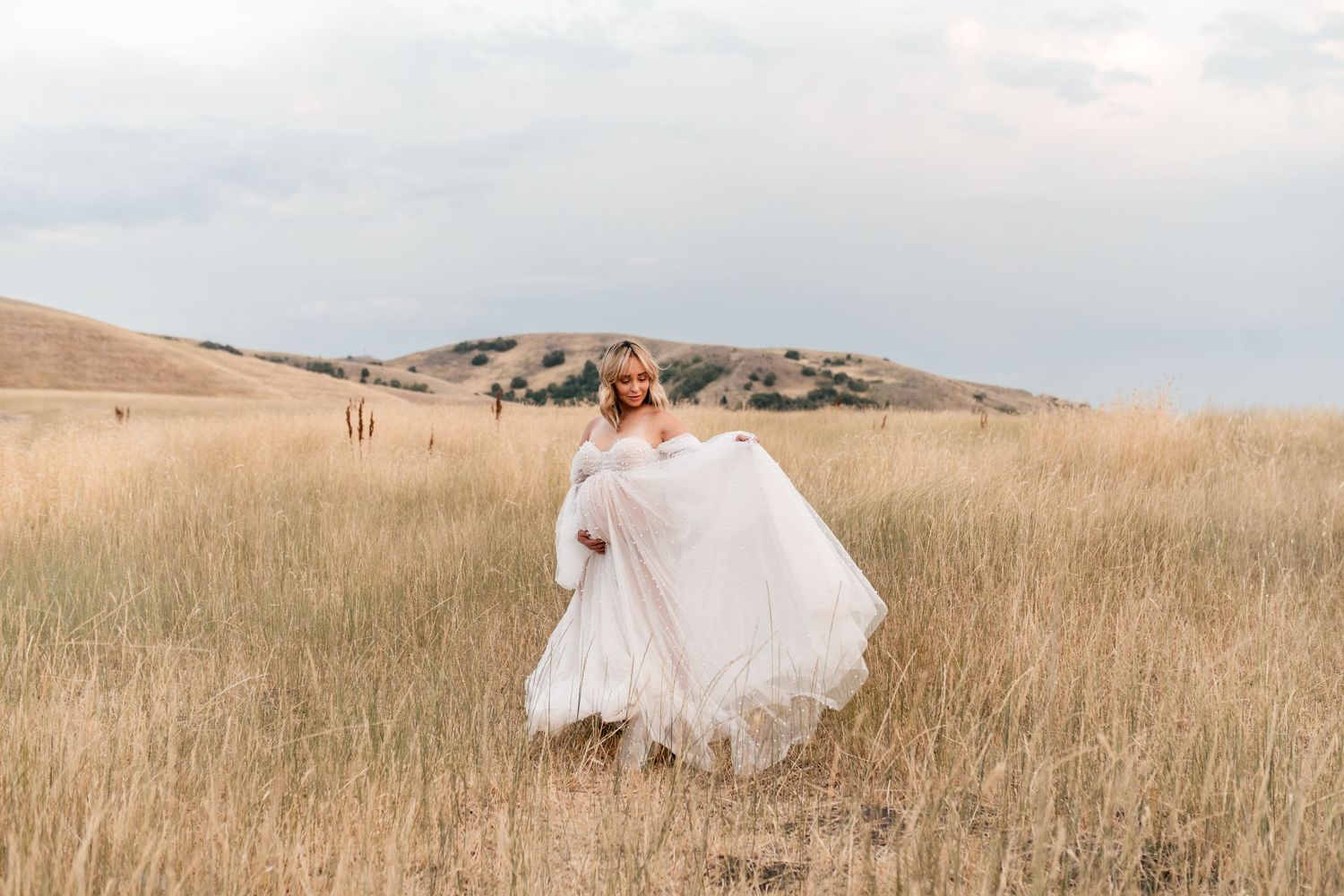 A bride in a flowing white gown walks through a golden wheat field at sunset creating a romantic silhouette.