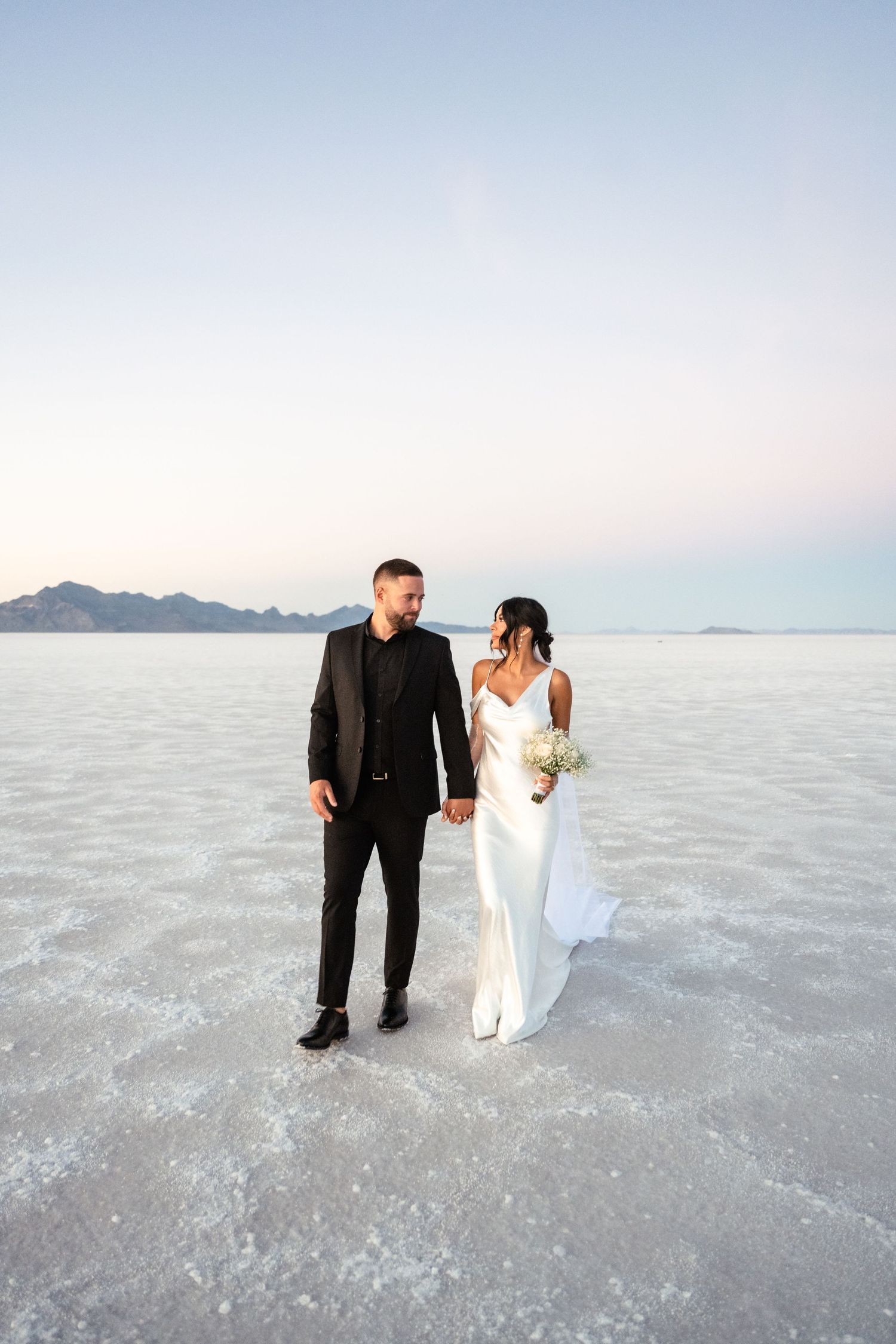 Wedding couple walking together on the stark white salt flats during a photo session.
