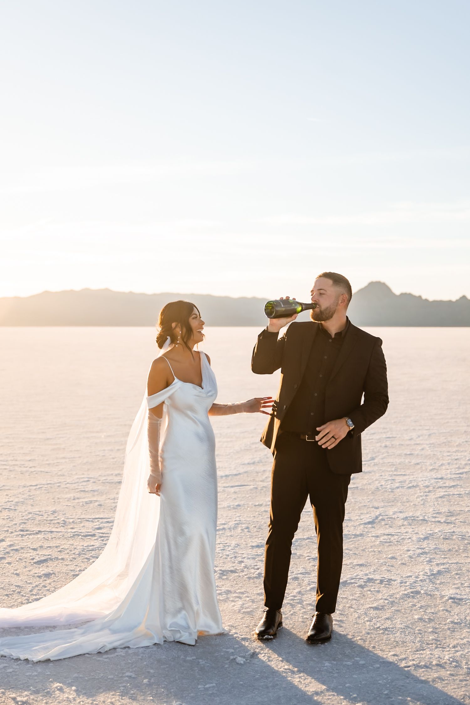 Wedding couple enjoying drinks together on scenic salt flats at sunset.