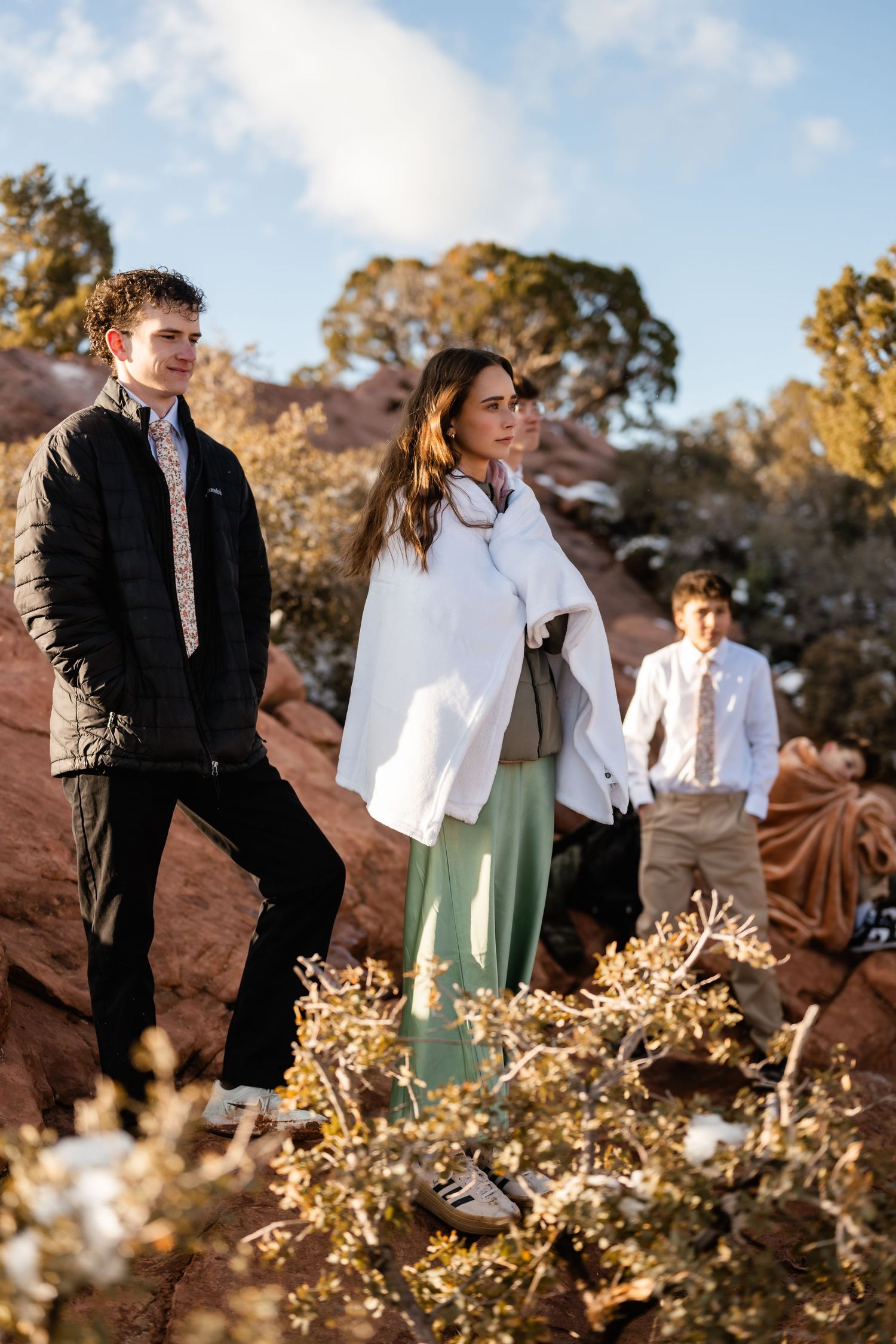 Wedding party poses among desert brush with red rock formations in background.