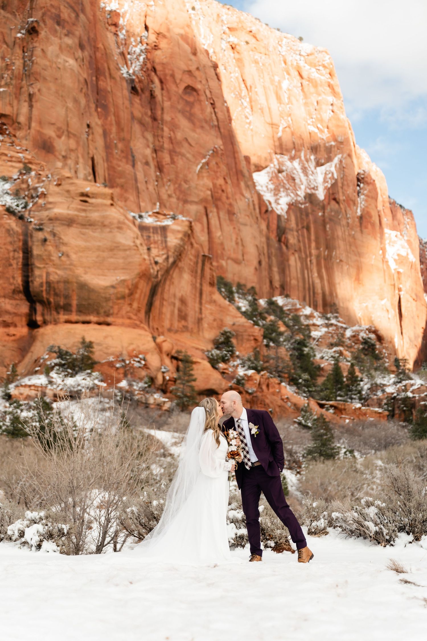 A romantic winter scene against towering red sandstone cliffs with patches of snow in the desert landscape.