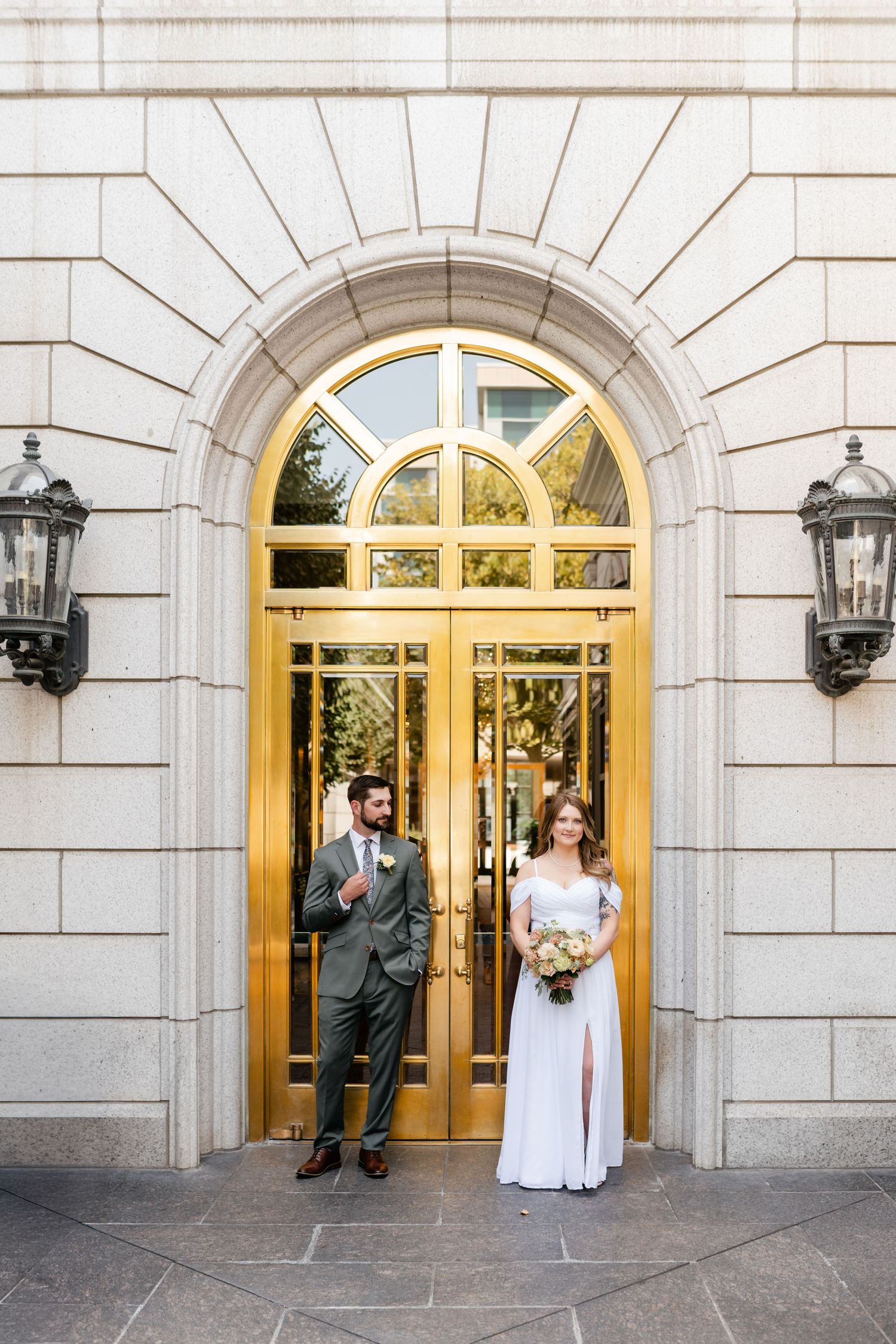 A couple poses in front of an elegant arched gold doorway with lanterns on a grand stone building.