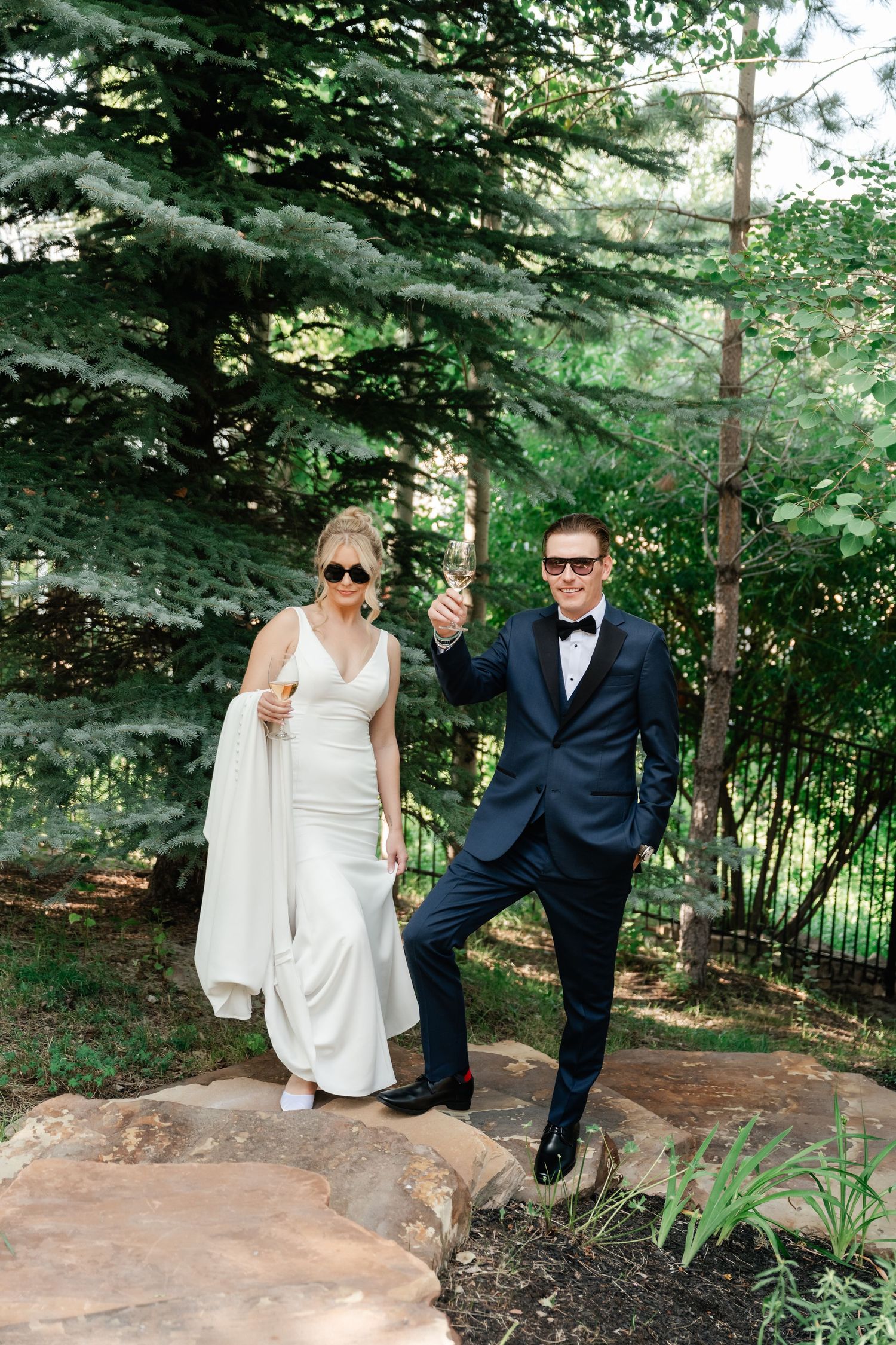 A couple shares playful moments together on stone steps surrounded by evergreen trees in a garden setting.