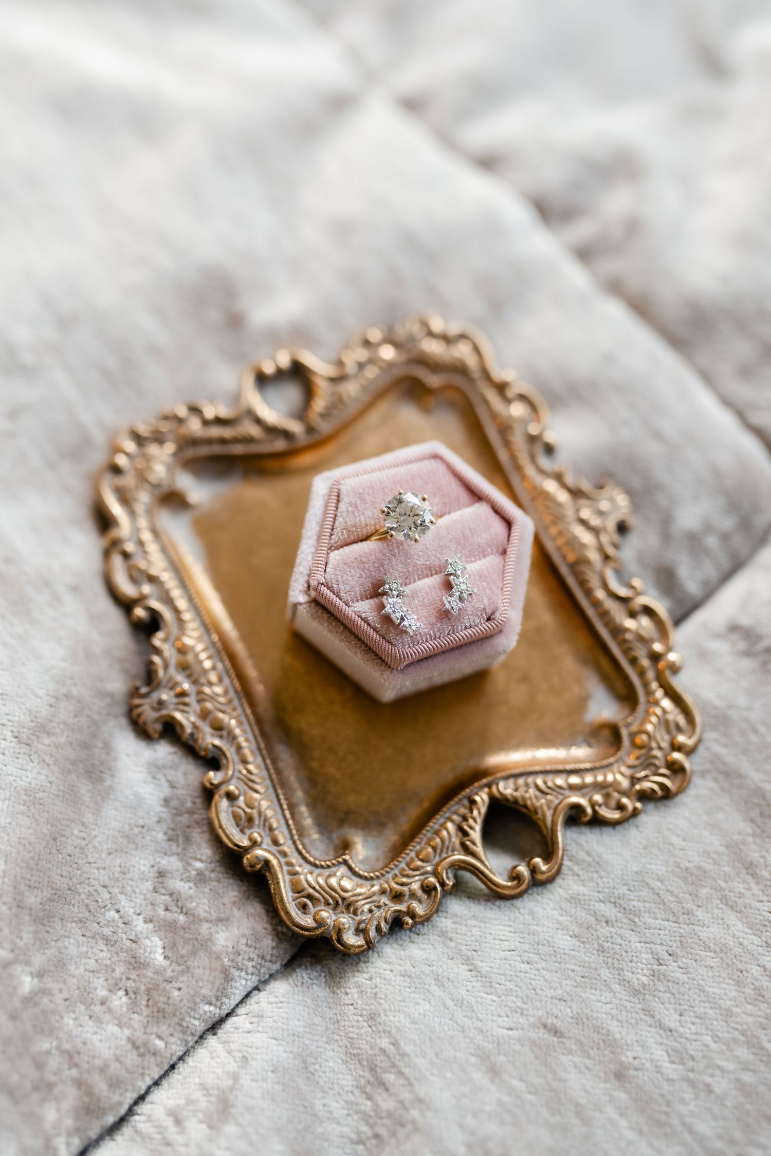 Vintage gold ornate frame holding pink ring box on stone surface.