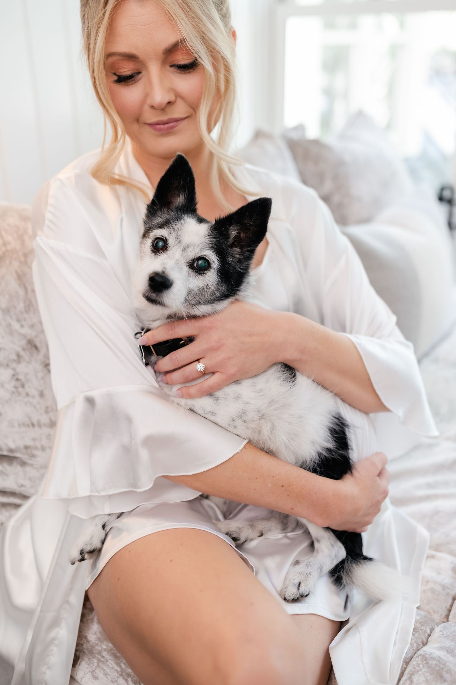 A black and white cat snuggles with someone wearing a white robe in a bright bedroom setting.