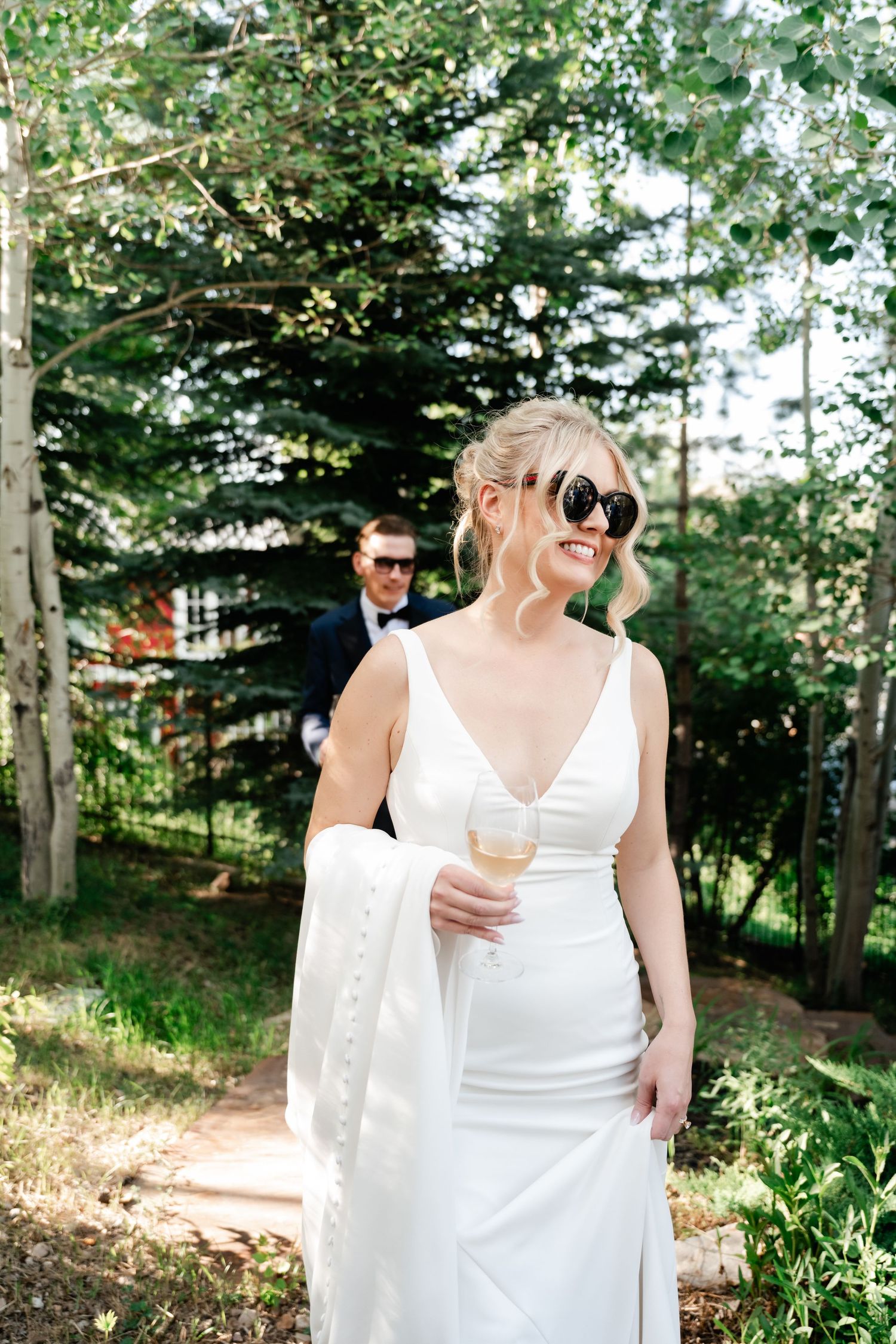 Wedding party enjoys candid moments in sunlit outdoor garden setting.