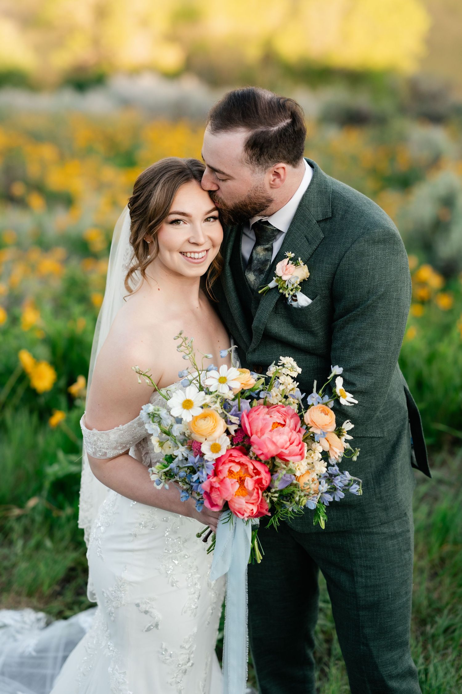 Romantic wedding portrait with colorful bouquet featuring coral peonies and daisies in mountain meadow.