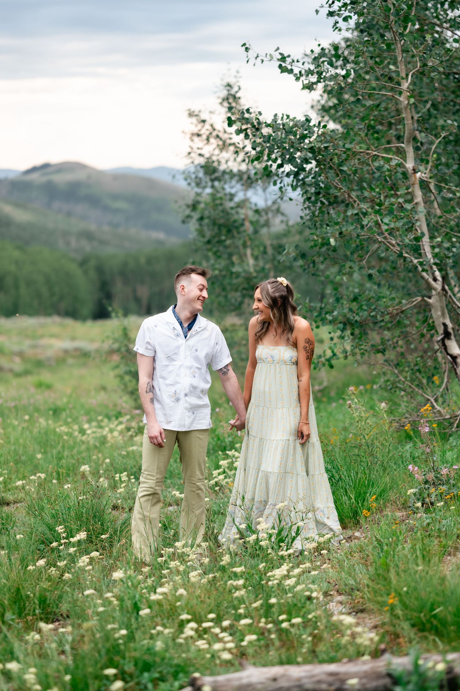 A couple strolls through a mountain meadow filled with wildflowers and aspen trees.