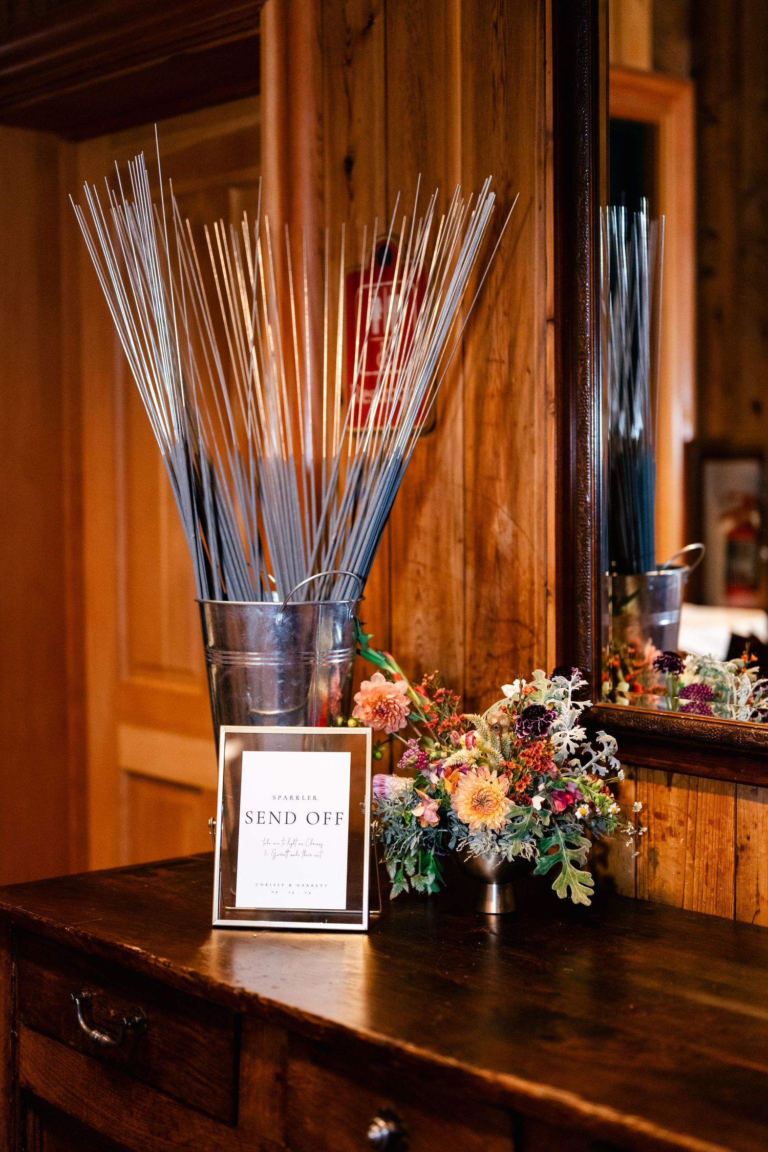 Sparklers arranged in glass vases with floral decorations on a wooden table at a wedding reception.