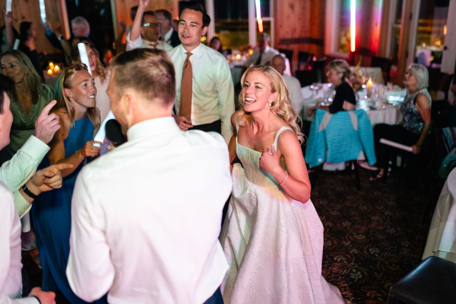 Wedding guests dancing and celebrating on a dimly lit dance floor at an evening reception.