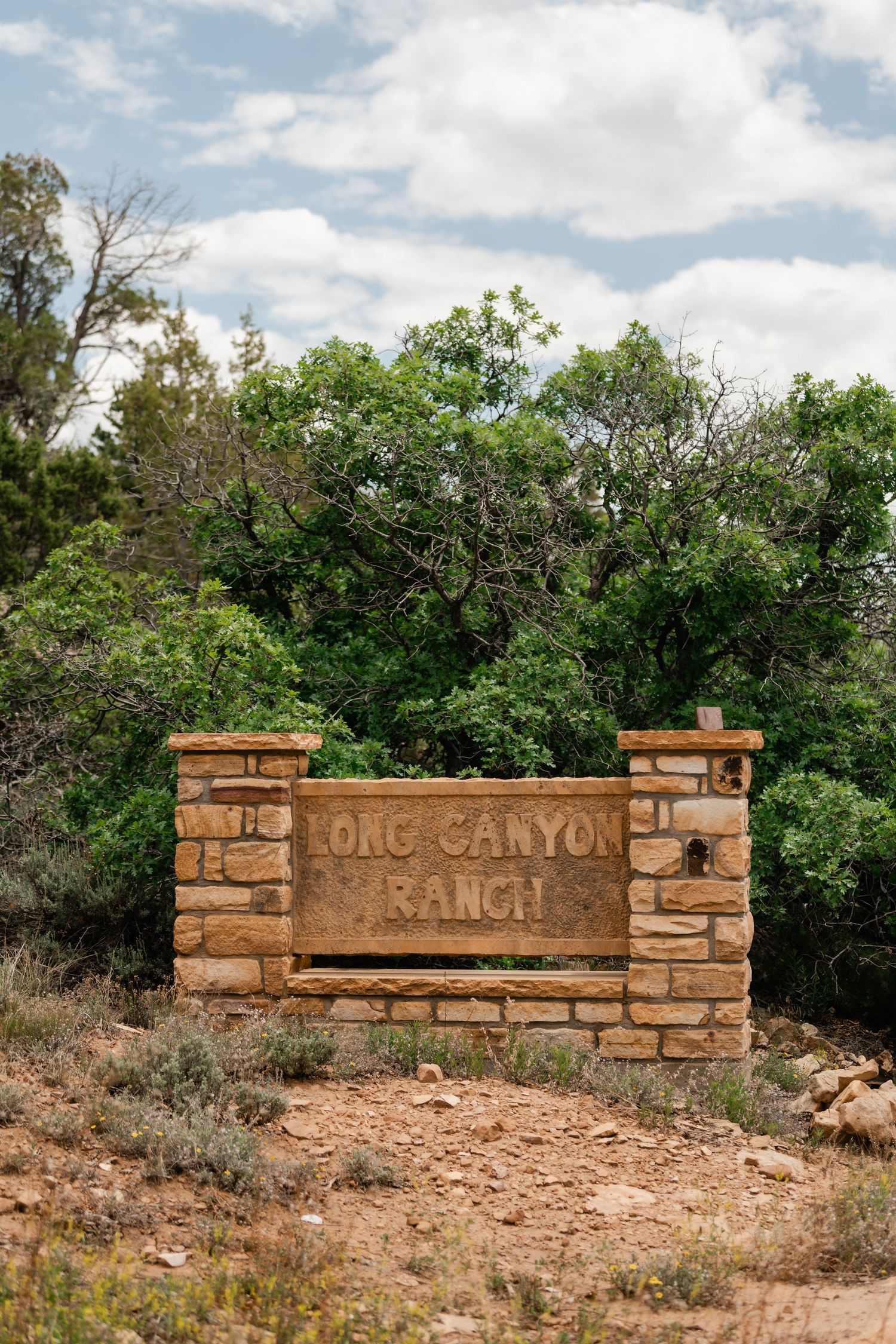 Stone entrance sign with rustic masonry wall surrounded by green foliage and natural landscaping.