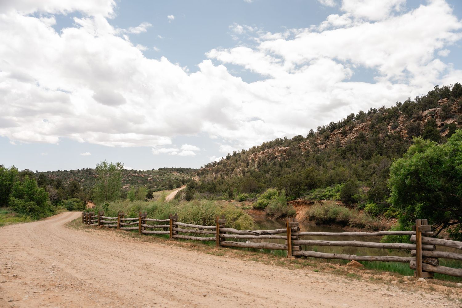 Scenic mountain landscape with split-rail fencing along a dirt path leading to rustic wooden structures.