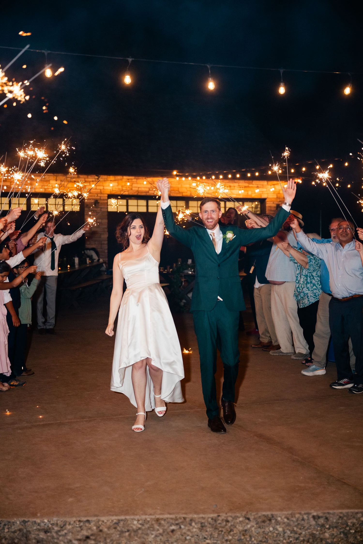 Wedding guests dance in formation under string lights during an evening celebration.