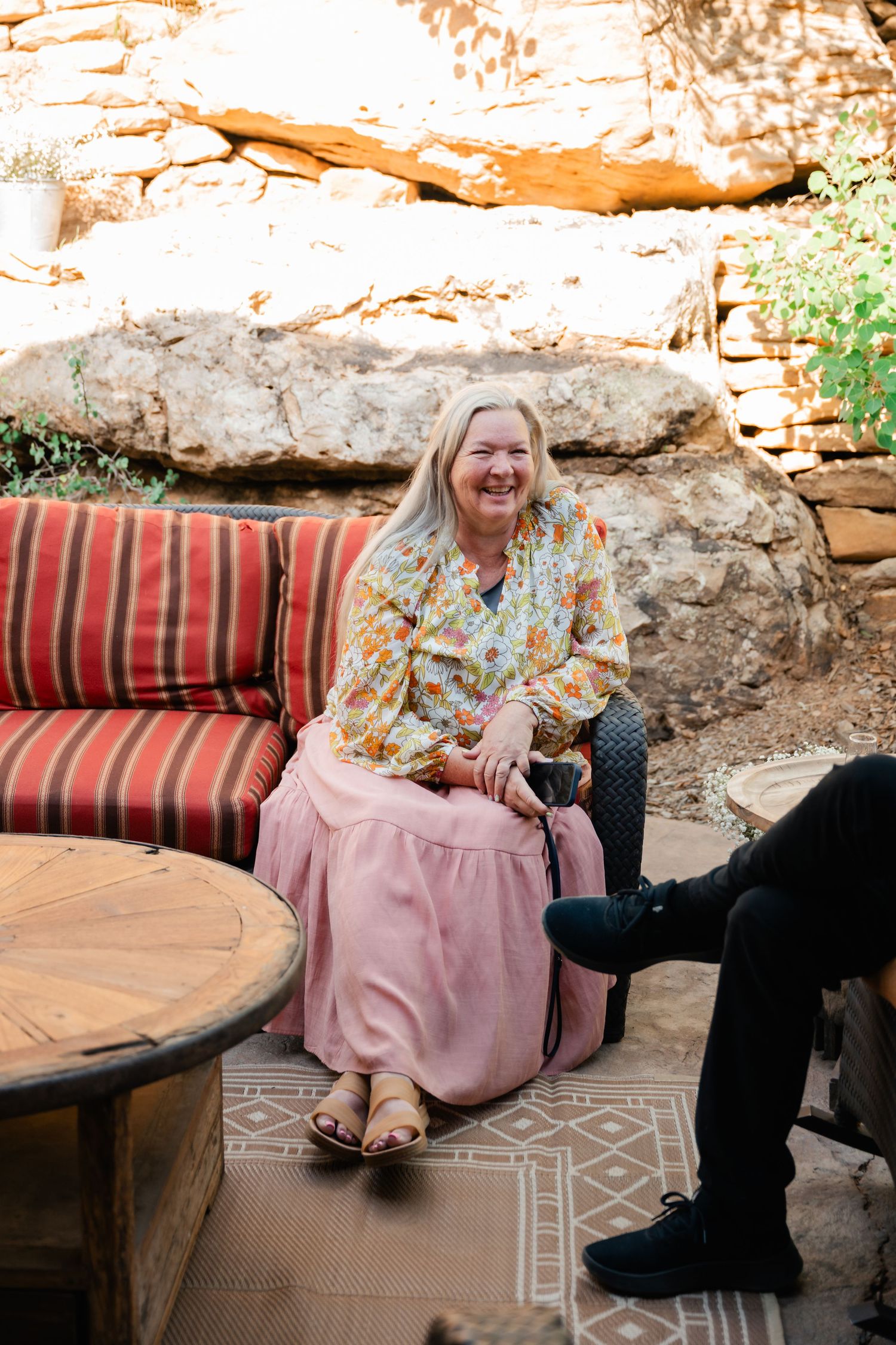 A person relaxing on cushioned outdoor seating against a rustic stone wall.