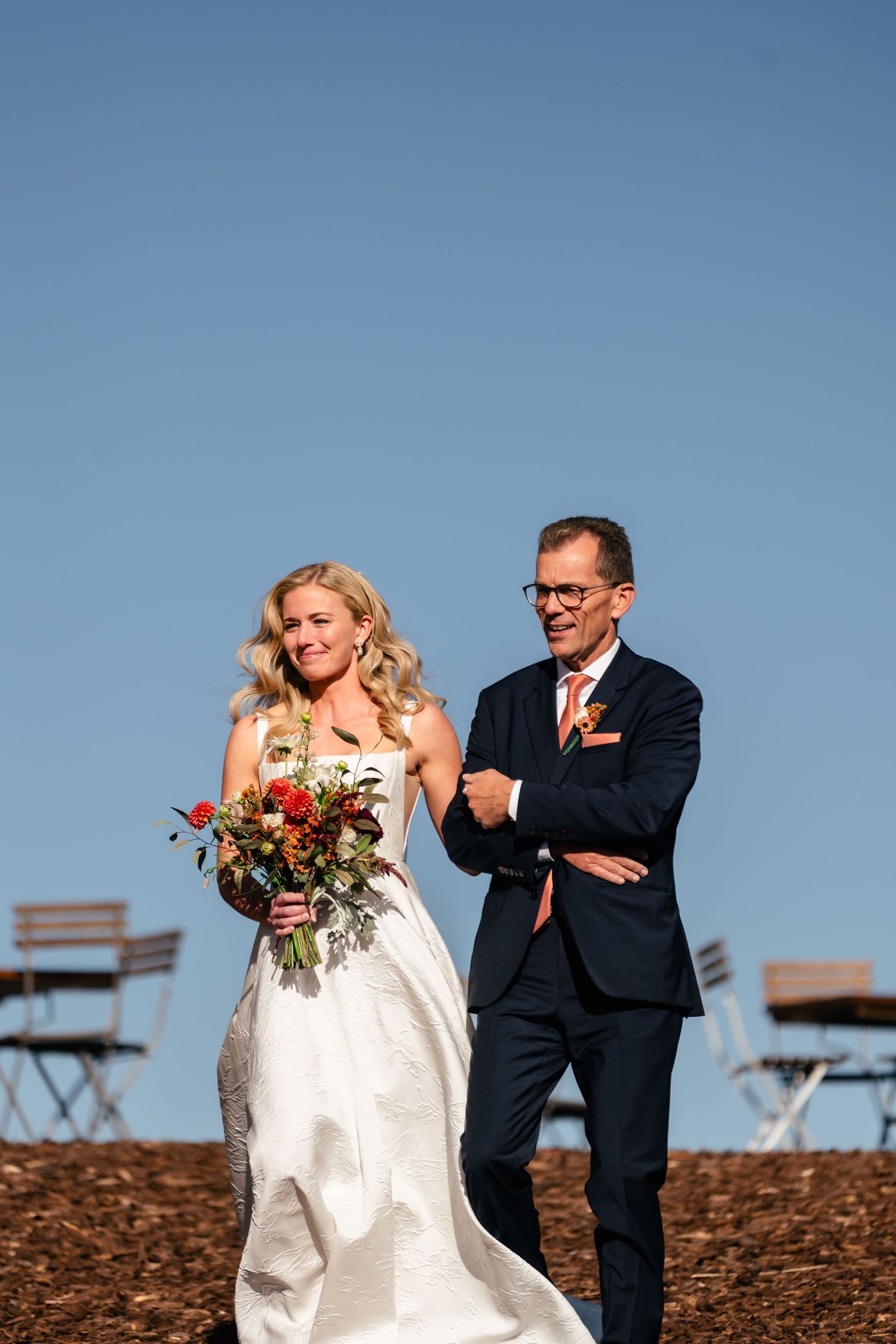 A couple at an outdoor wedding ceremony, with the bride in a white dress holding a colorful bouquet against a blue sky. Park City Wedding.