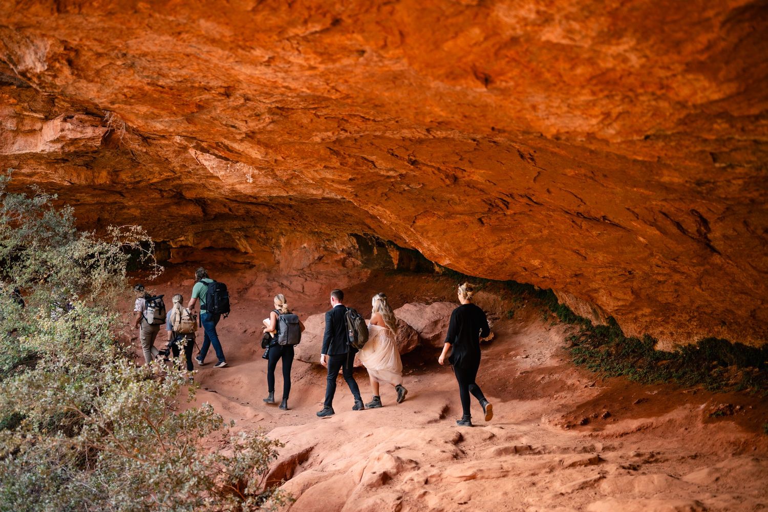 A wedding party explores a red rock cave formation during an outdoor ceremony.