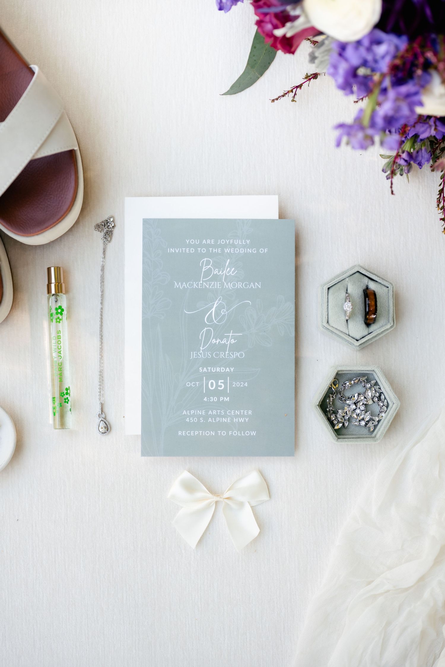 Wedding invitation with grey card and floral decor alongside decorative elements and accessories on white surface.