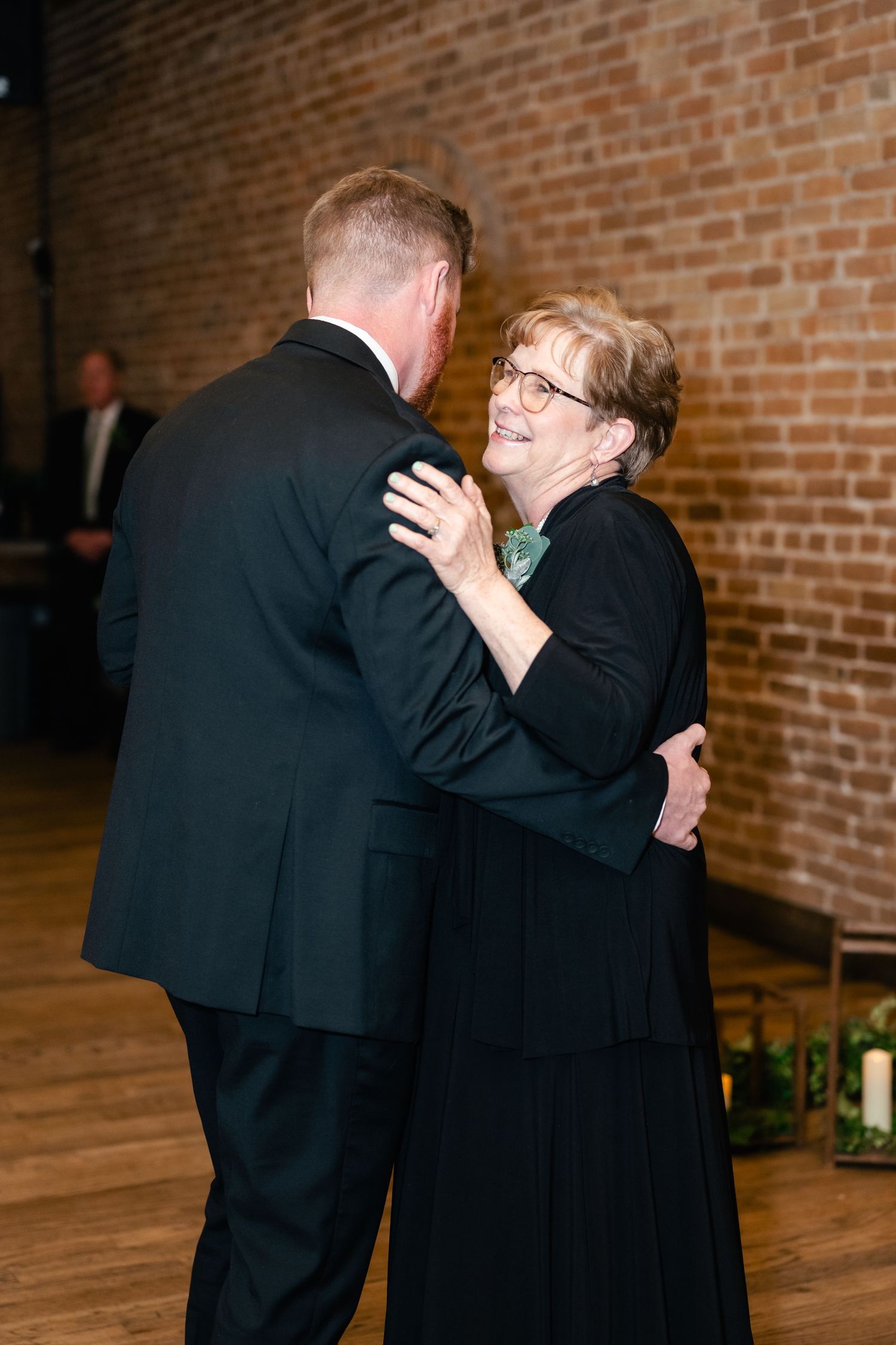 A mother-son dance at a wedding reception shows a heartfelt moment between them on a wooden floor against exposed brick walls.