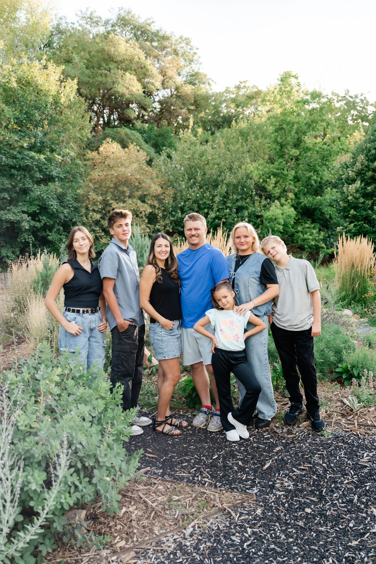 A group poses together outdoors on a garden path surrounded by lush greenery and ornamental grasses.