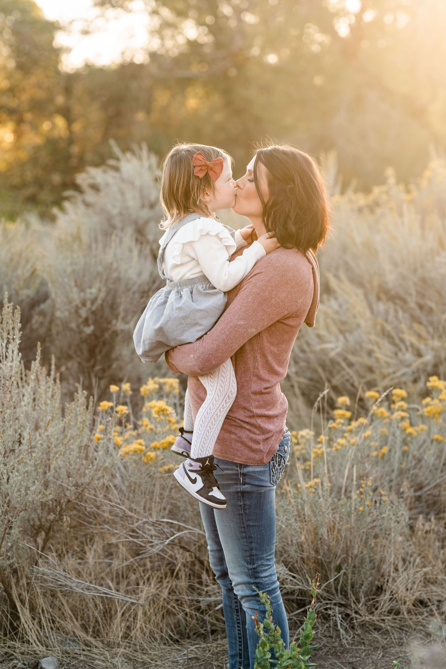 A tender family moment captured in golden sunlight with tall grasses and wildflowers in the background.