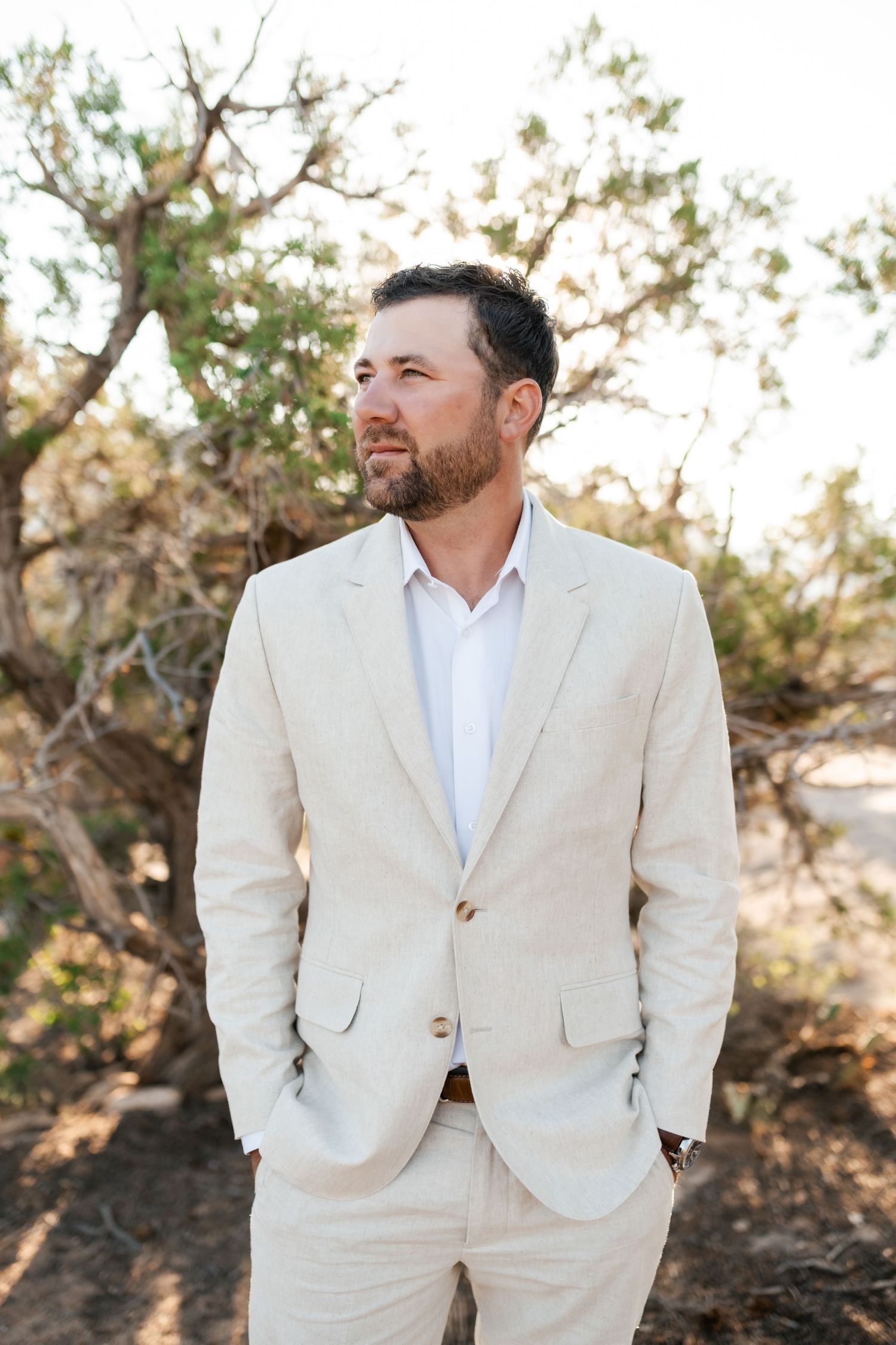 Zion destination photographer, Groom in light beige suit poses in desert setting with natural lighting.