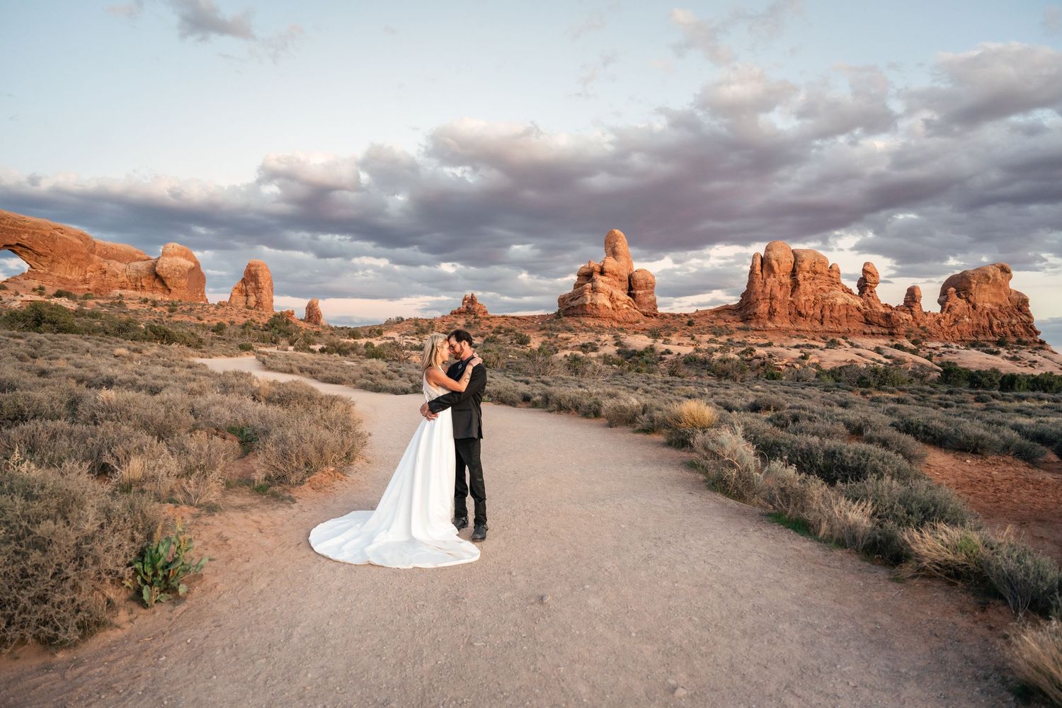 Desert landscape with dramatic red rock formations and cloudy skies at Arches National Park during golden hour.