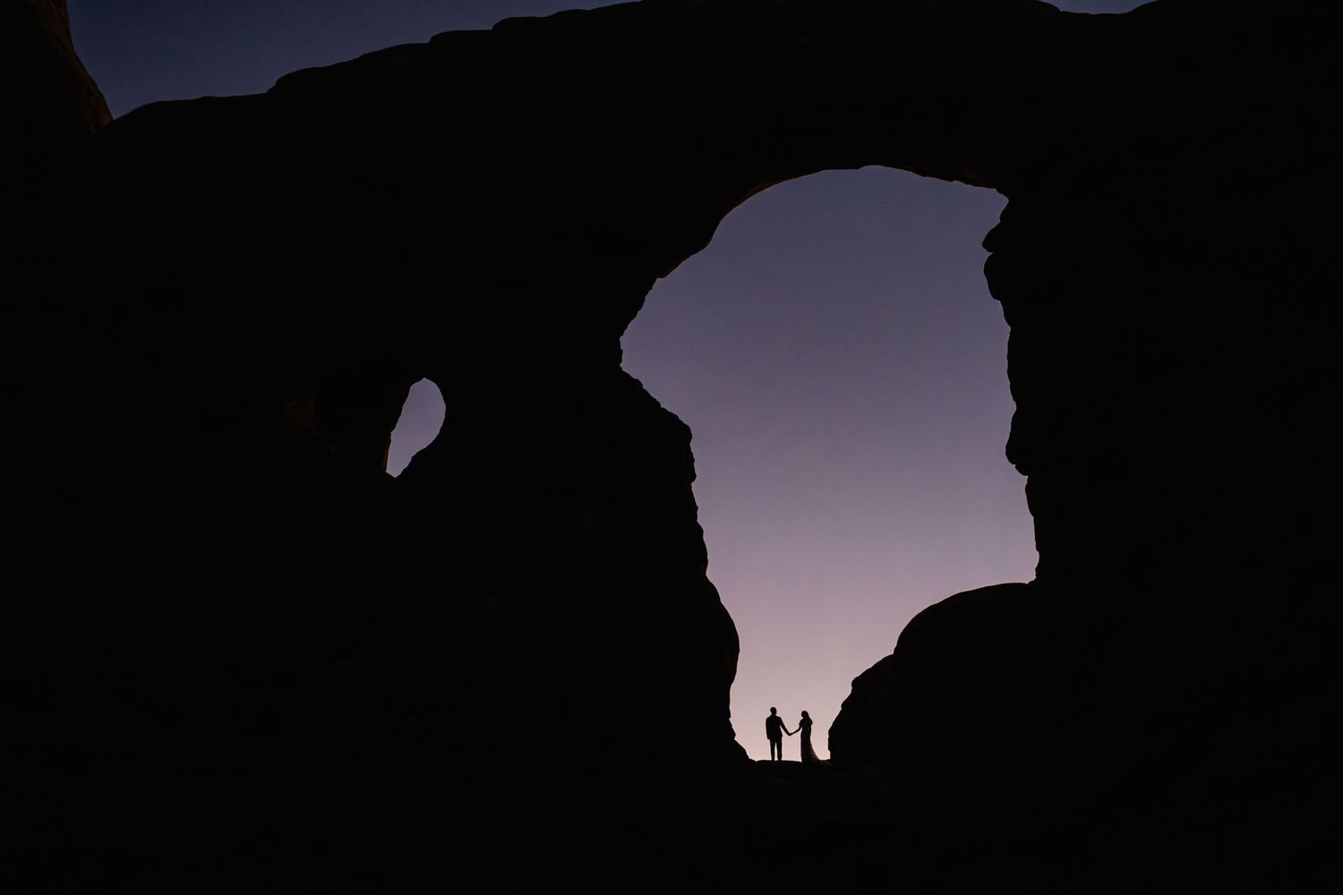Silhouetted figures stand against a purple sunset sky creating a dramatic panoramic view.