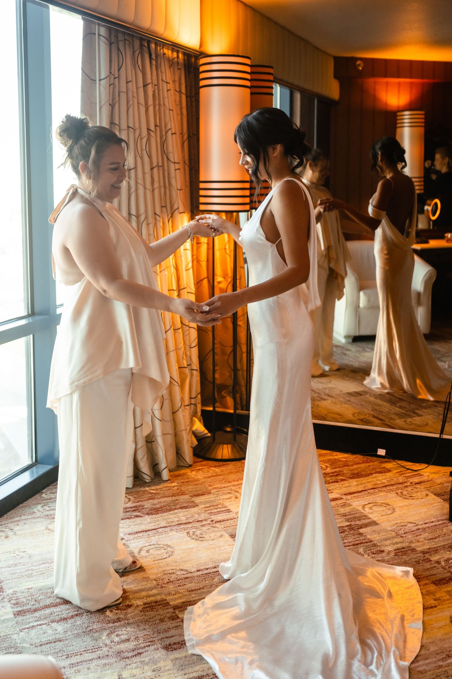 A flowing white wedding dress being fitted and adjusted in an elegant hotel setting.