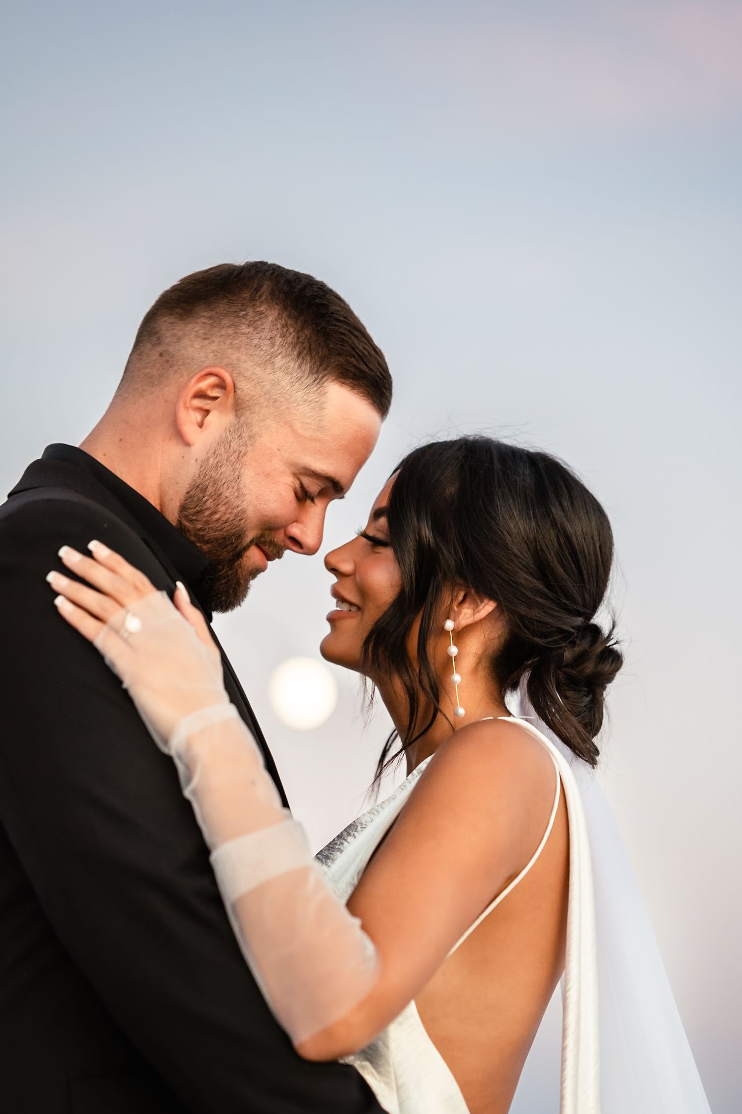 Intimate wedding portrait moments captured against soft pastel sky.