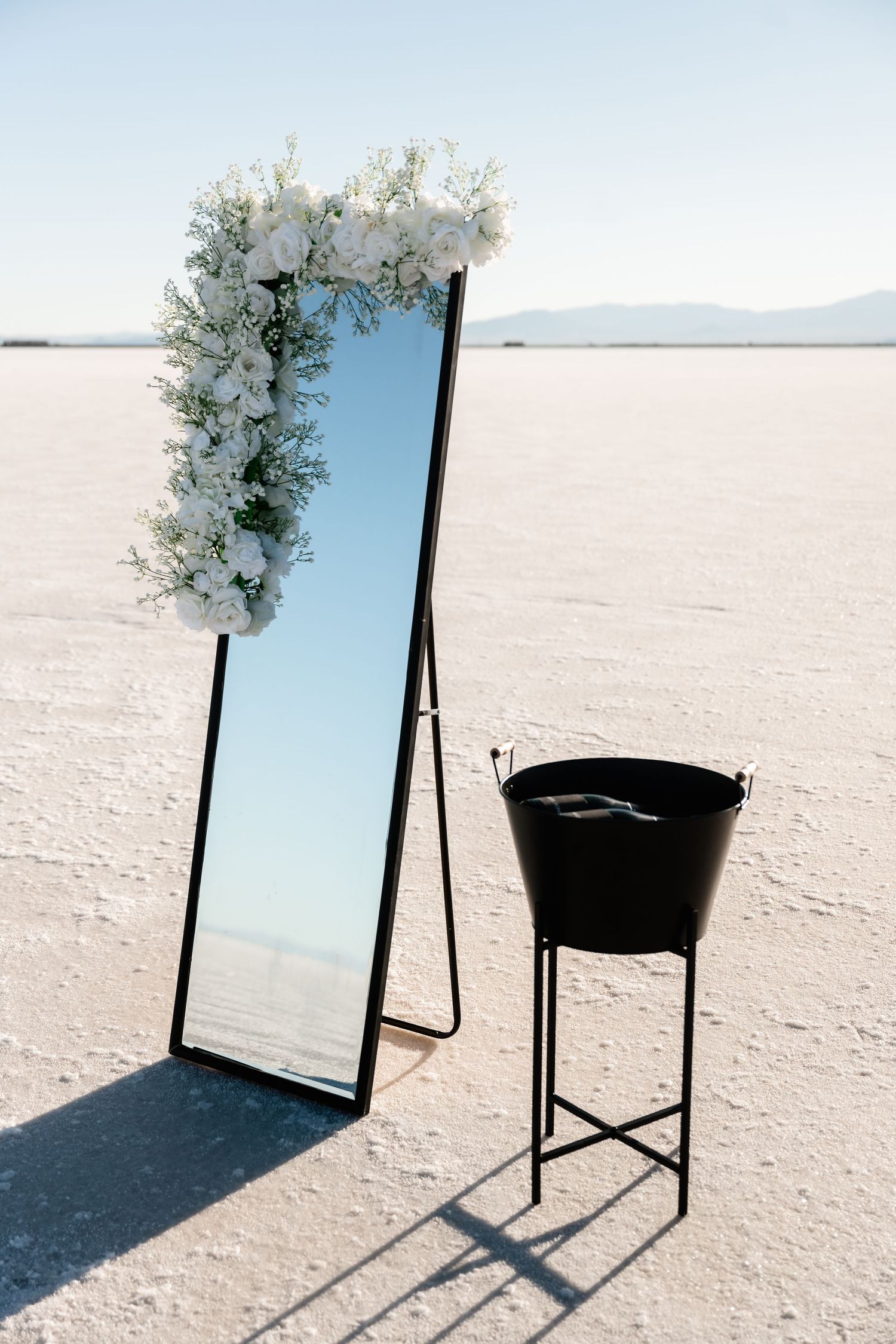 Minimalist wedding setup with white floral arrangements and mirrors on a stark white salt flat landscape.