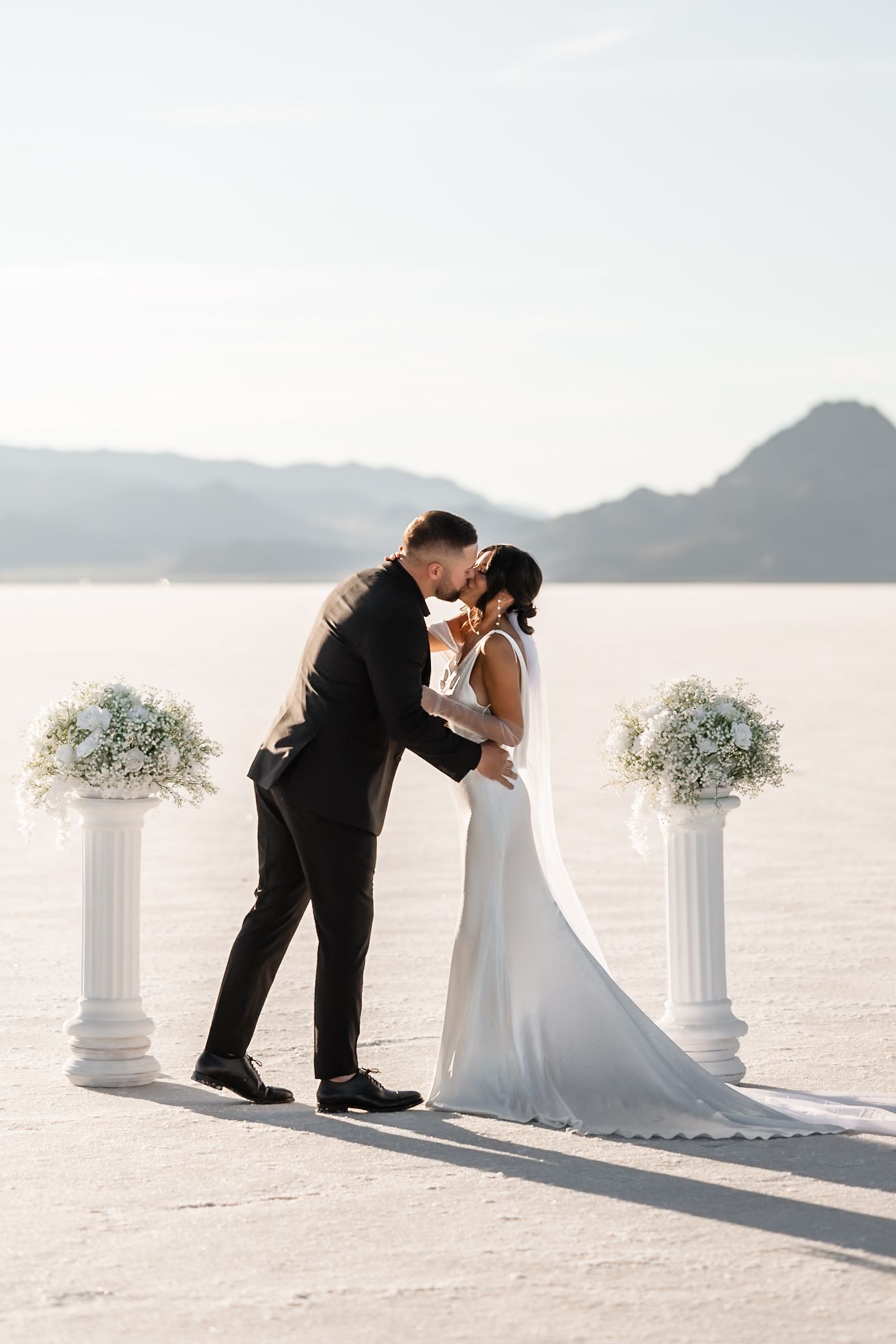 Romantic wedding moment captured on salt flats with white floral pedestals.